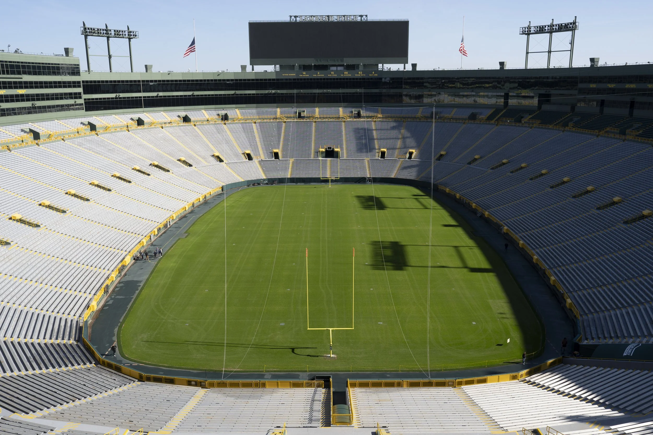 Empty football stadium with green field, yellow goalposts, and surrounding seats, under clear sky.