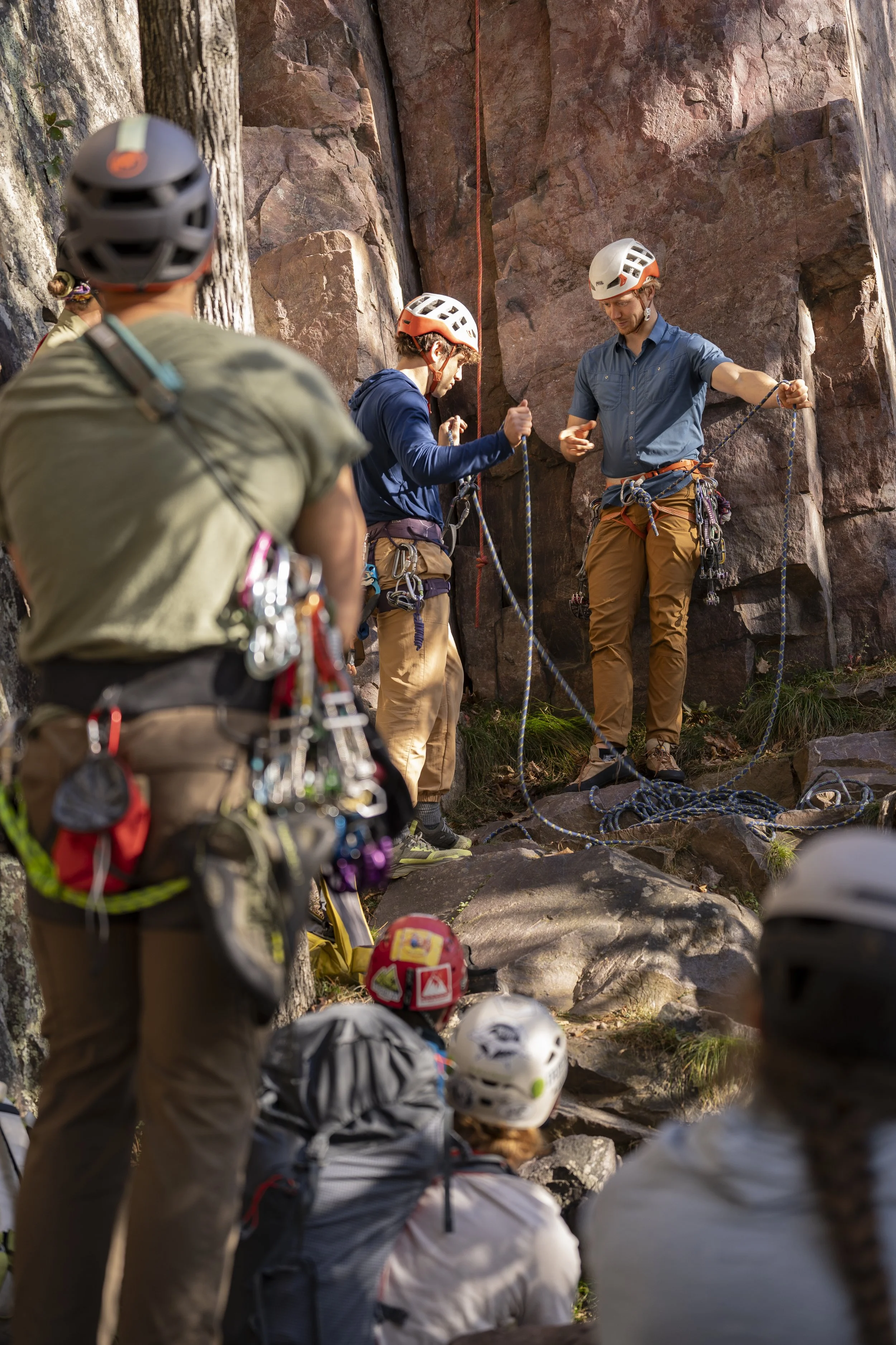Group of rock climbers preparing for a climb on a quartzite rock face, with instructors explaining safety procedures.