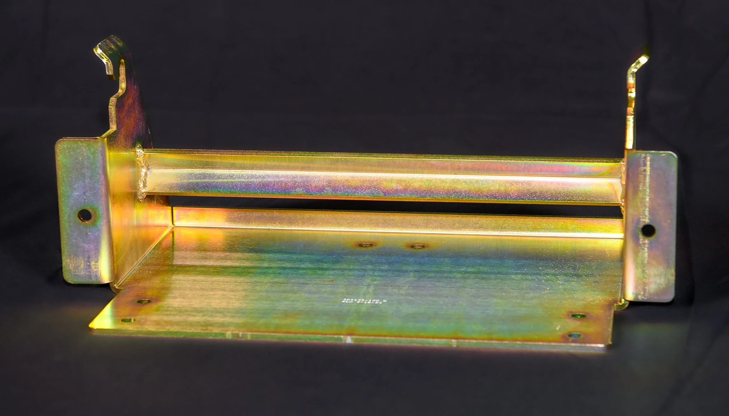 A metallic, yellow-golden, L-shaped bracket with multiple holes and a rail in the middle, likely used for mounting or support in a machine or electronic device.