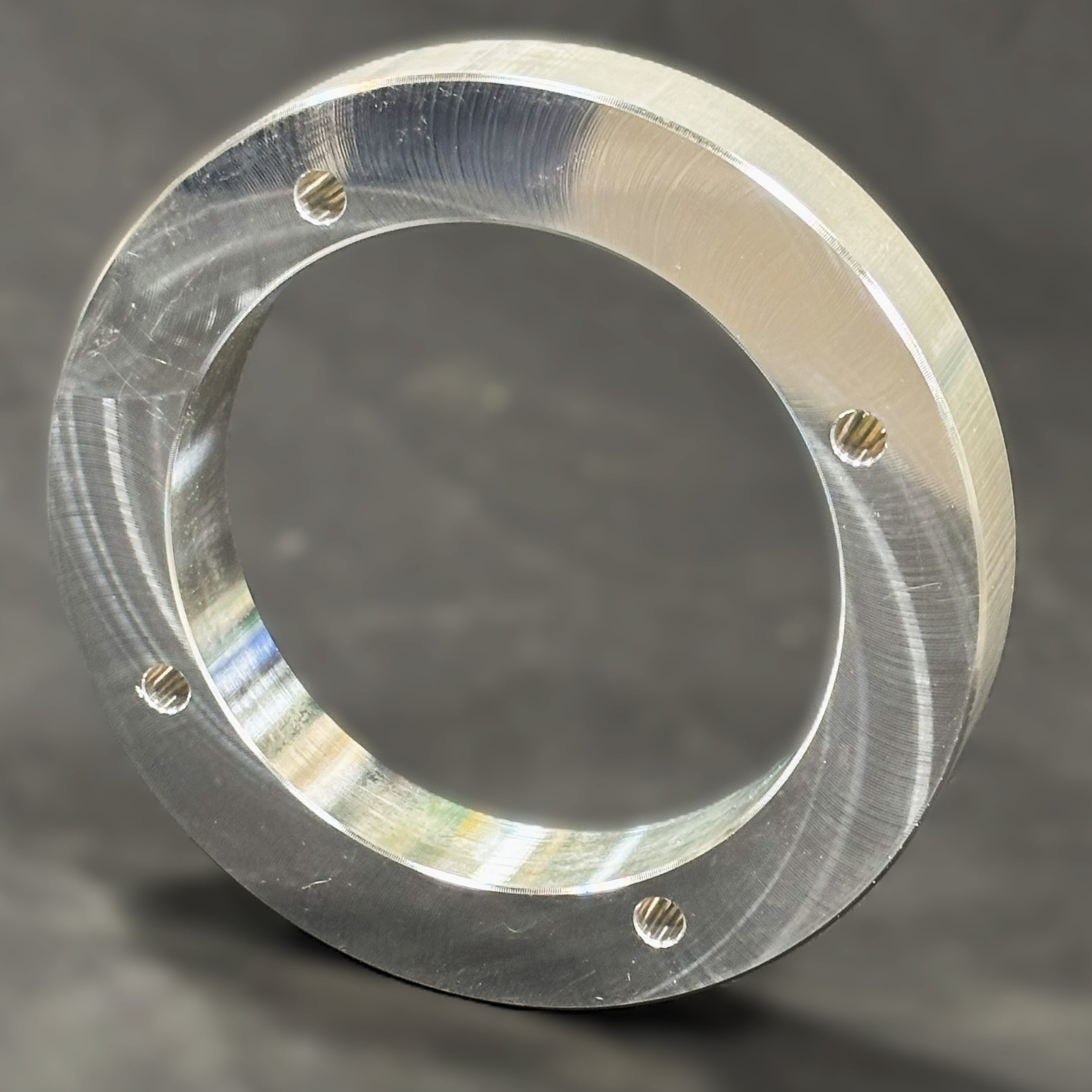 Close-up of a metallic circular flange with four evenly spaced screw holes.
