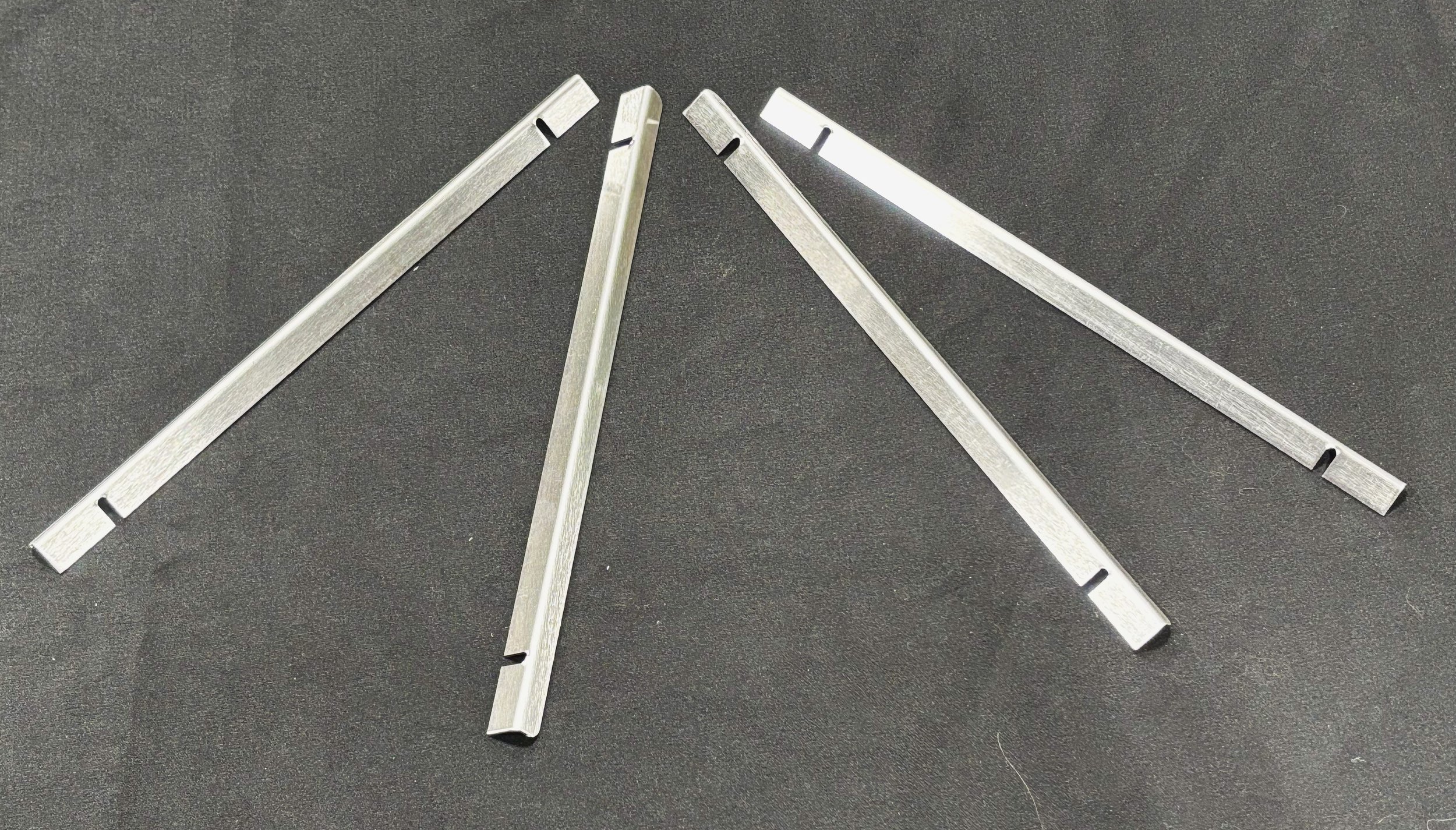 Four metallic tools with flat, elongated bodies and notched ends, arranged on a black surface.