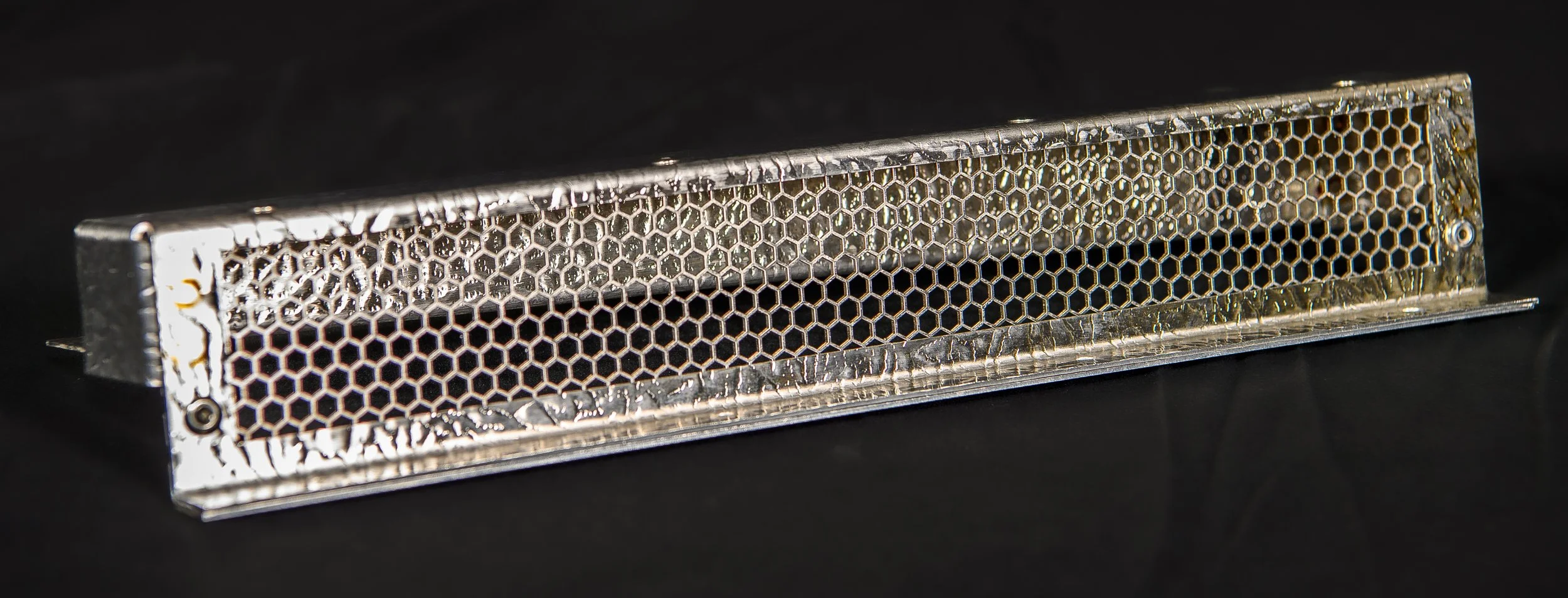 A metal honeycomb-like grid attached to a metallic frame, resting on a black surface.