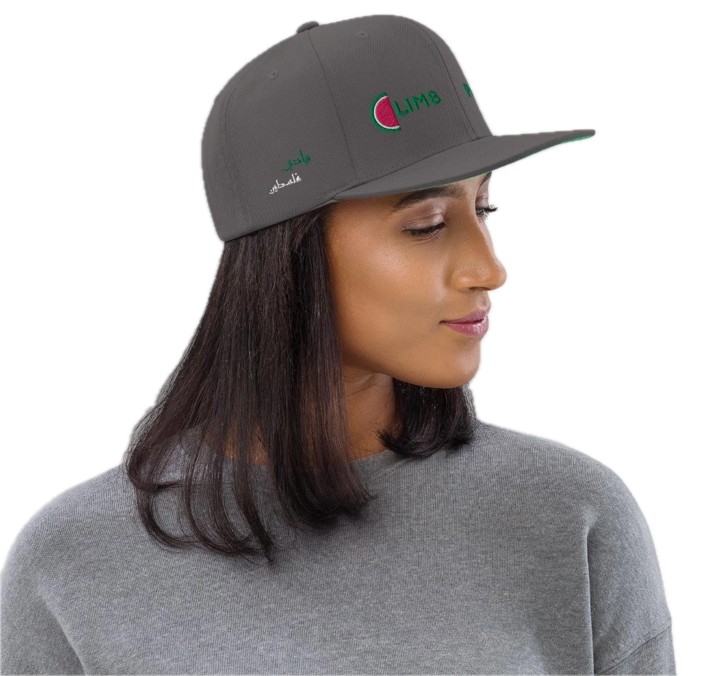 A woman wearing a gray baseball cap with the logo and Arabic text, looking to her right, wearing a gray sweatshirt.