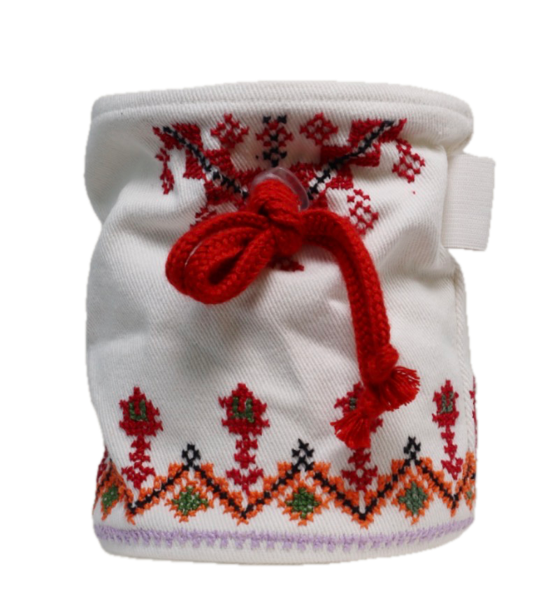 A white cloth item with red and black cross-stitch embroidery, tied with a red yarn bow, featuring decorative patterns including diamonds and floral motifs.