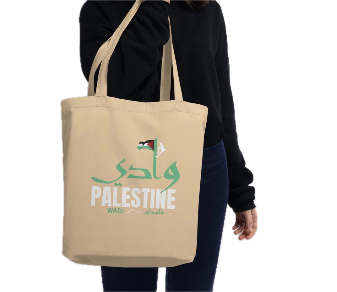 Person holding a beige tote bag with the words 'Welcome Palestine' written in Arabic and English, and the Palestinian flag.
