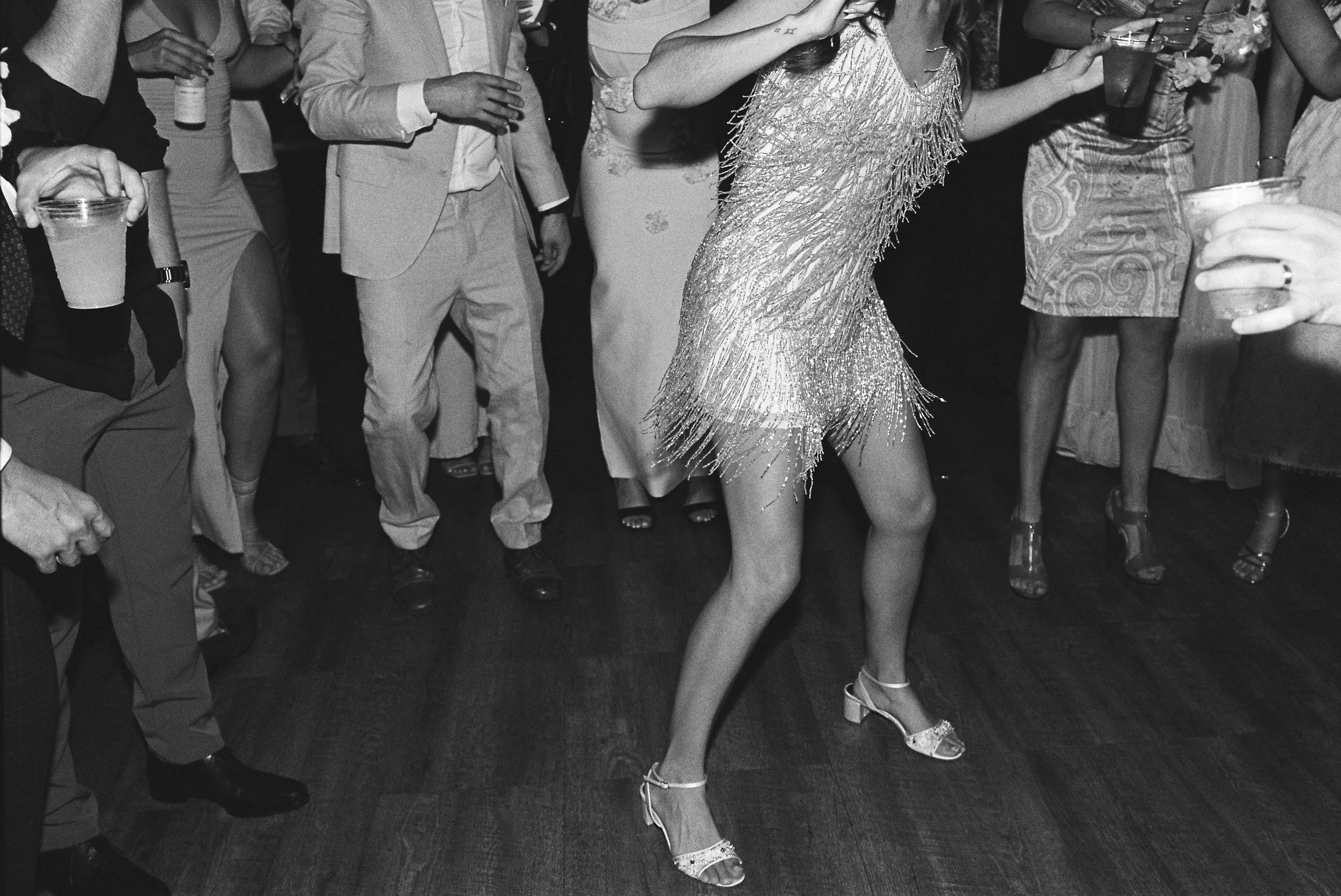 A woman dancing in a sparkly dress and heels at a party, surrounded by people holding drinks.