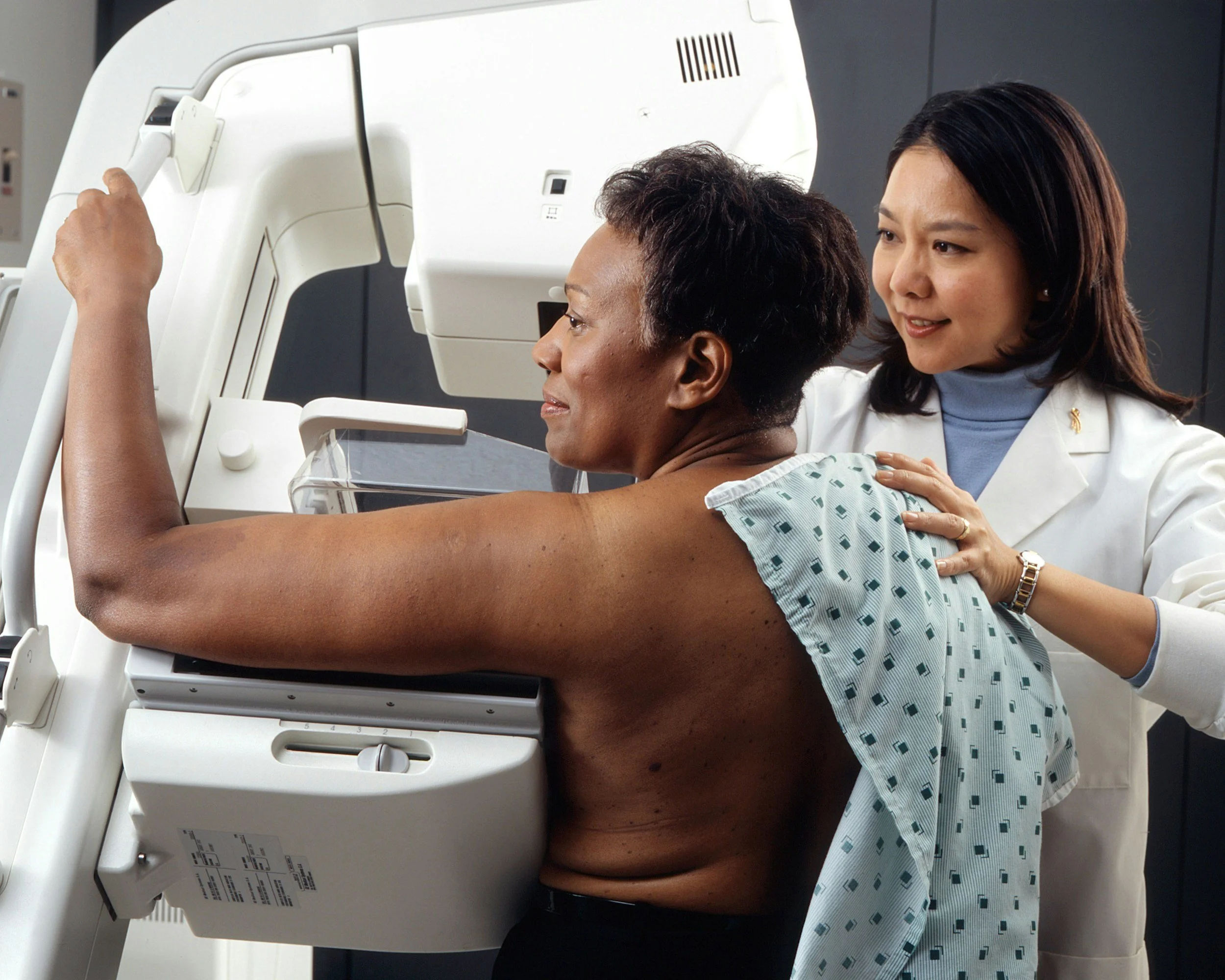 Black middle-aged woman with short hair getting mammogram by asian technician