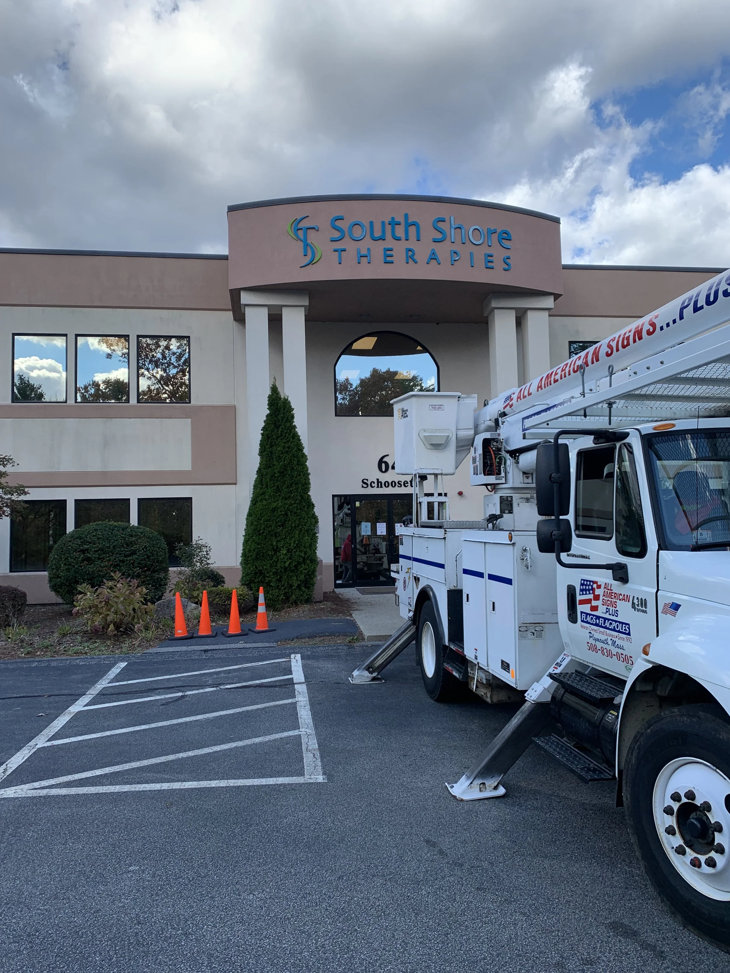 Exterior of South Shore Therapies building with a vehicles for sign installation parked outside and orange traffic cones nearby.