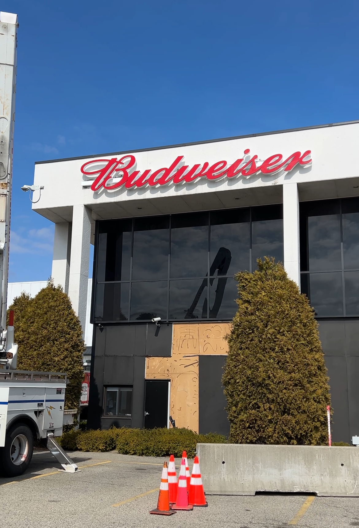 Two photos of a storefront building with a large red 'Budweiser' sign, a white exterior, large windows, and a black garage door. Construction equipment and cones are visible in the first image.