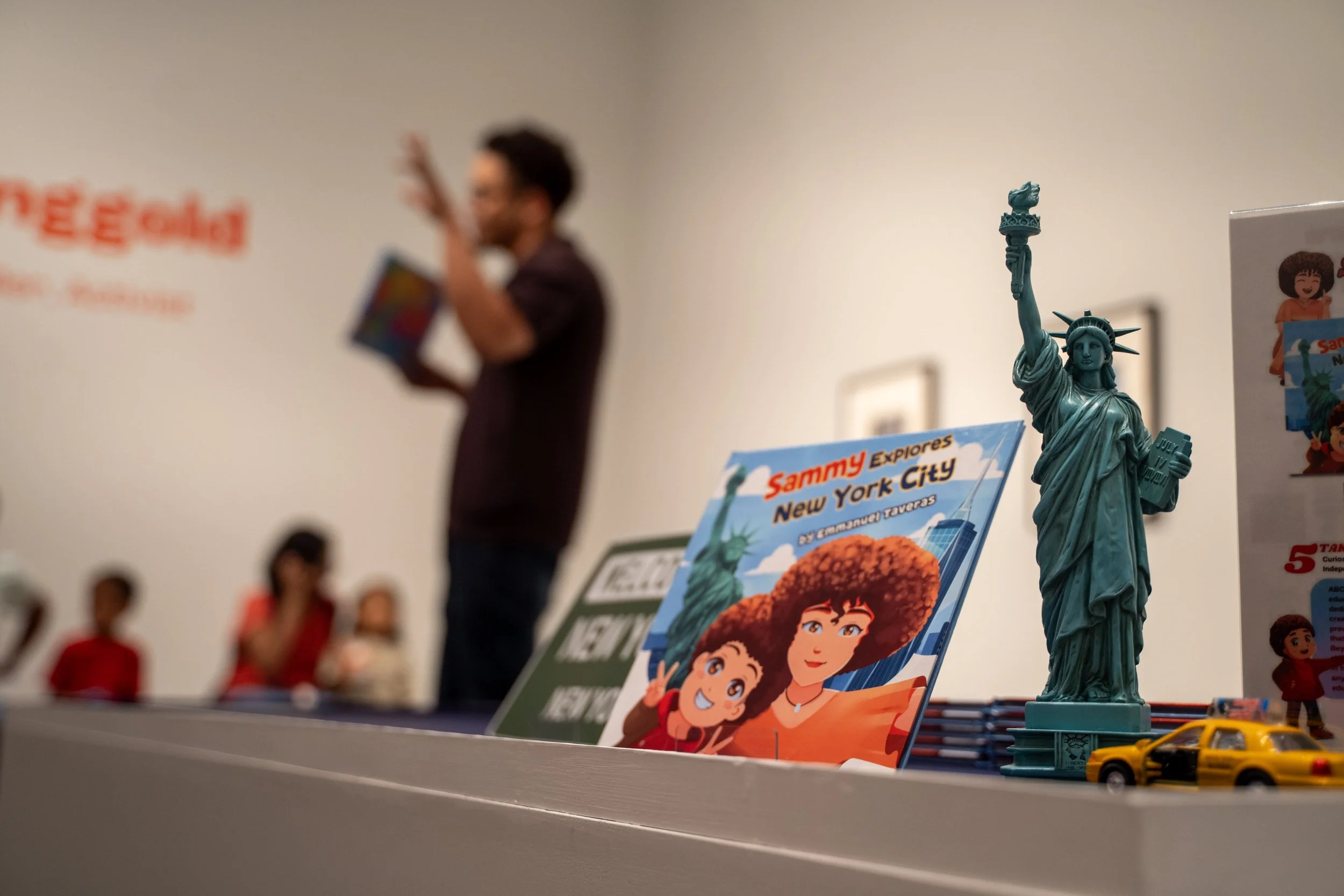 Children's New York City book, Statue of Liberty figurine, and yellow taxi model on a museum display shelf