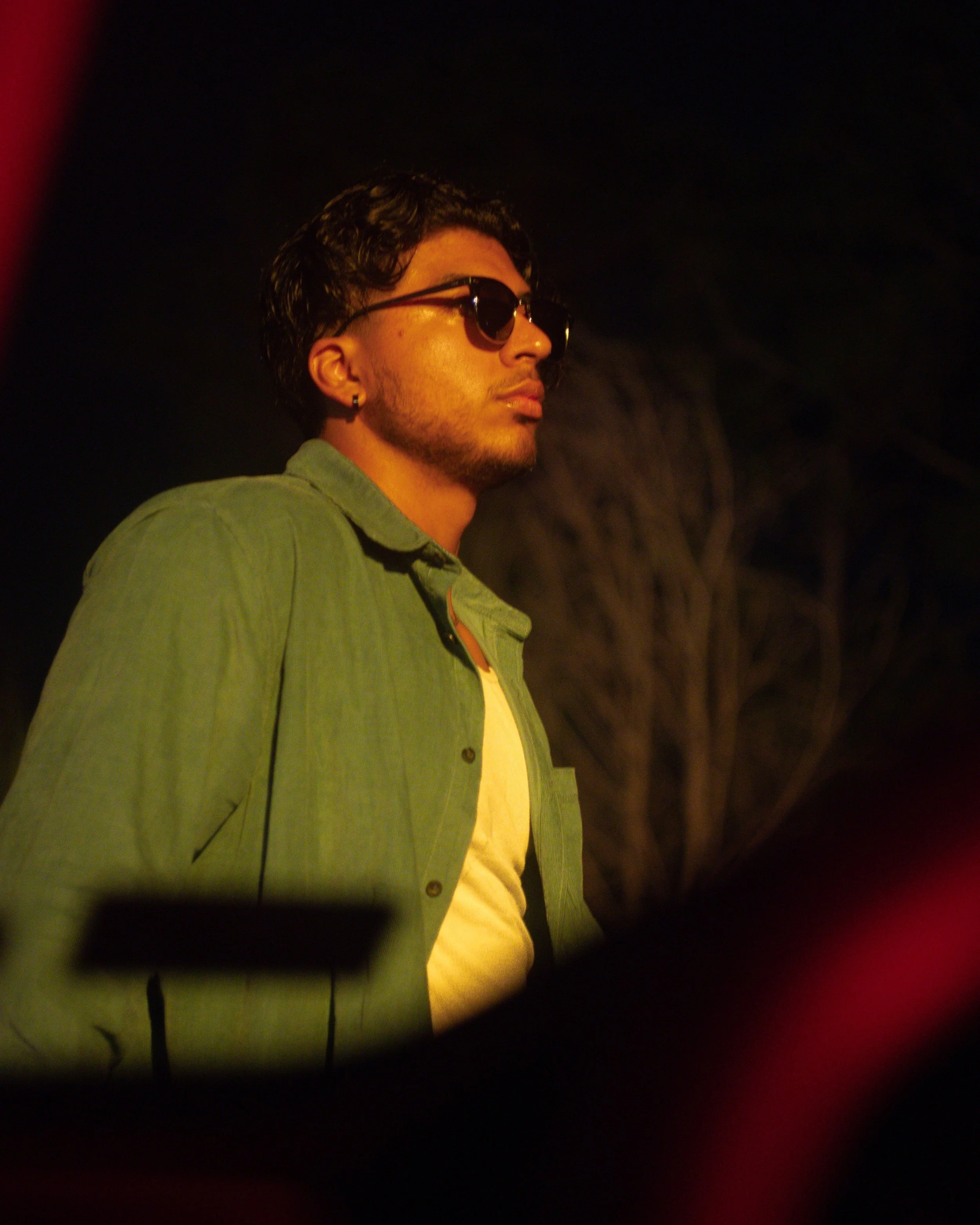 Person wearing sunglasses and a green shirt, standing outdoors at night for portrait photography.