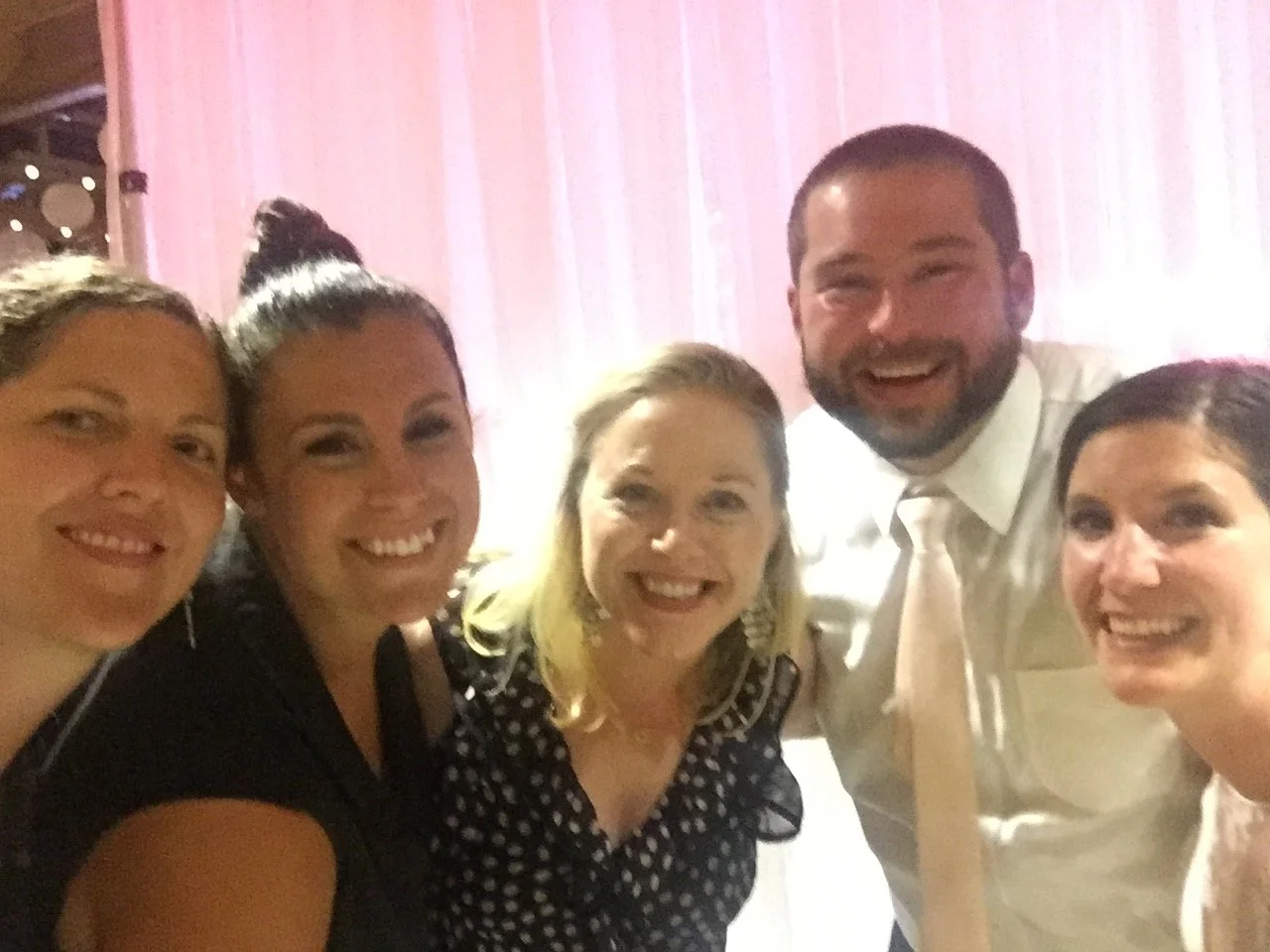 Group of five people smiling at a party or event, with a pink backdrop.