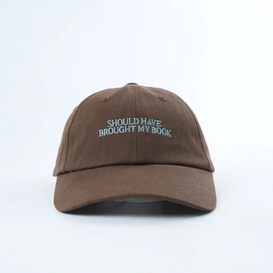 Brown embroidered bookish dad hat featuring the phrase “Should Have Brought My Book” in white lettering, curved brim and adjustable fit for readers and book lovers.