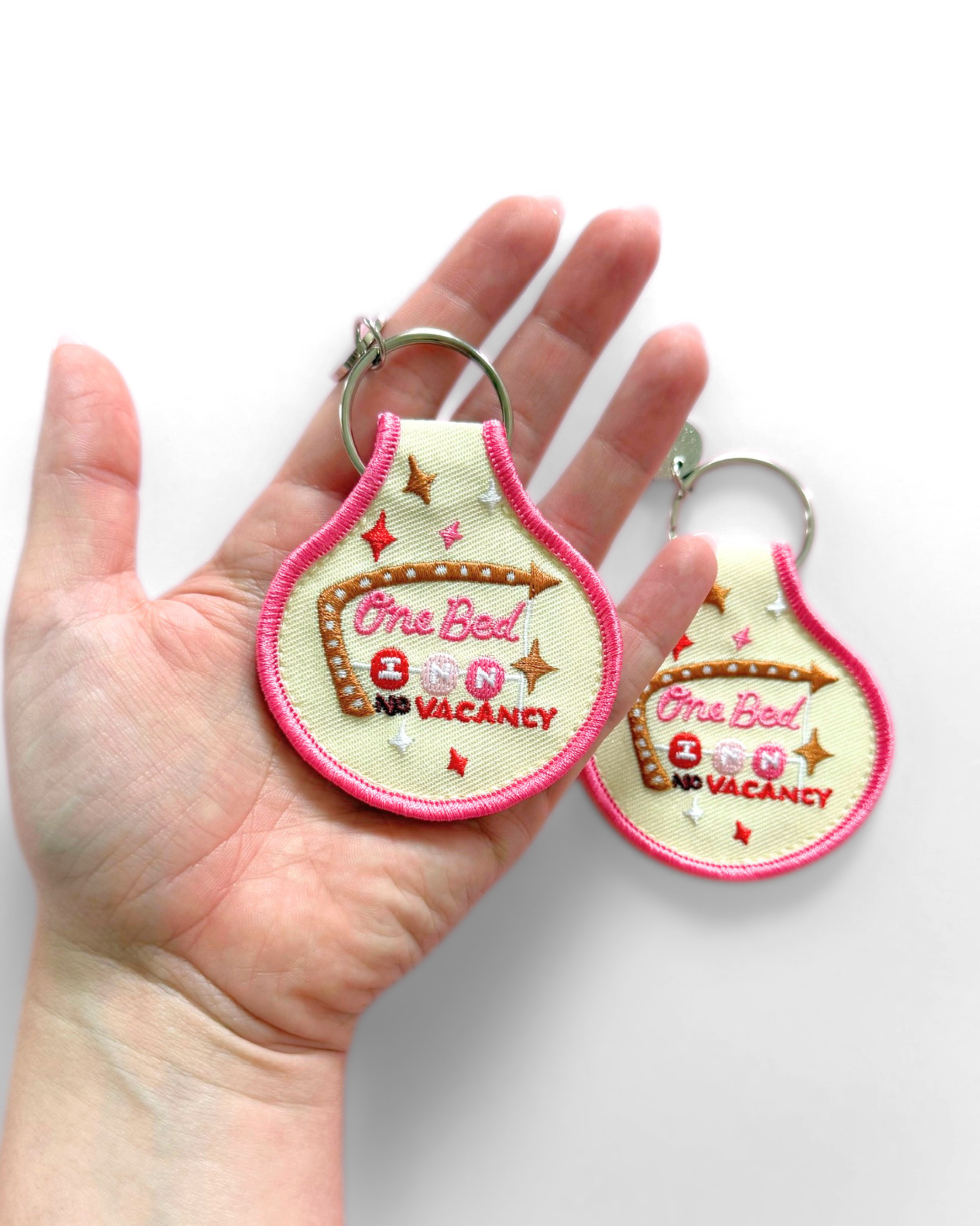 Cream embroidered fabric keychain with hot pink trim featuring a retro motel-style “One Bed, No Vacancy” design with colorful stars and silver key ring.