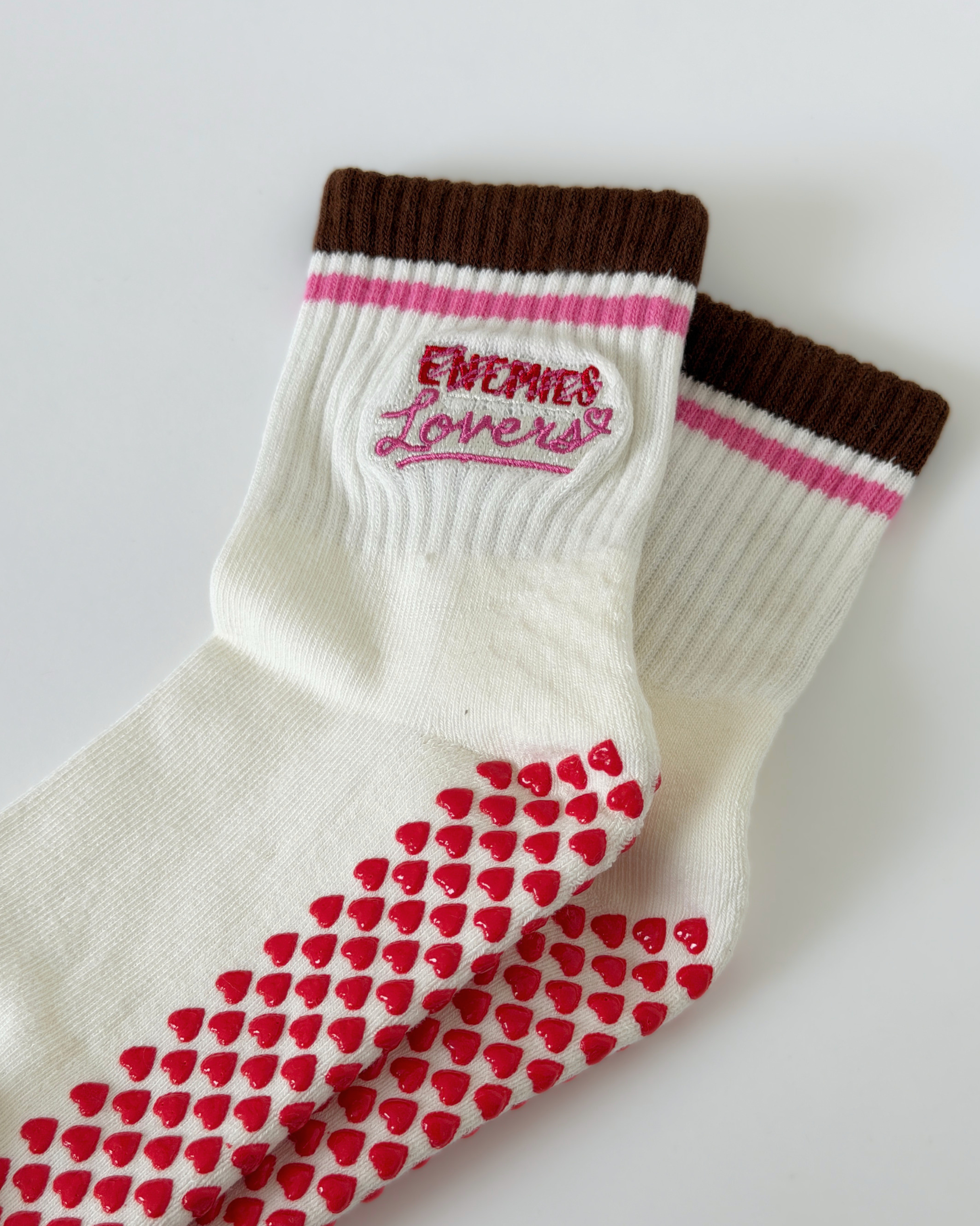 Stripe ankle sock in majority white that says Enemies crossed out Lovers with red heart grips