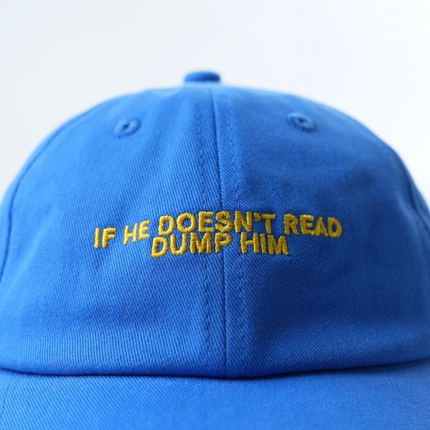 Bright blue cotton dad hat featuring yellow embroidered text that reads “IF HE DOESN'T READ DUMP HIM.”