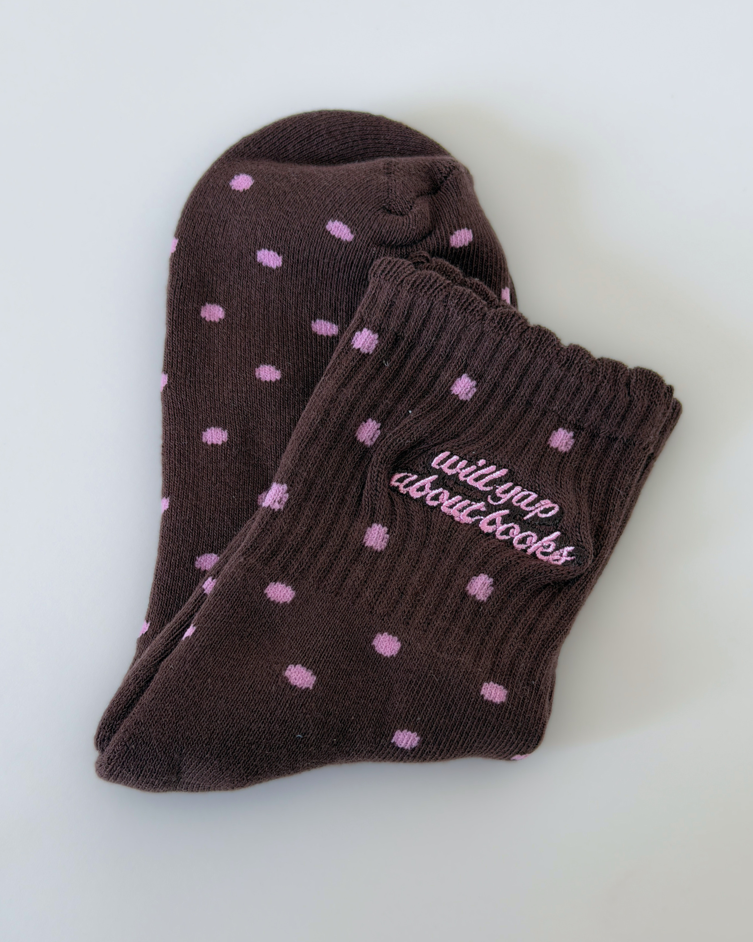 Brown sock with pink polka dots that say Will Yap About Books in embroidery