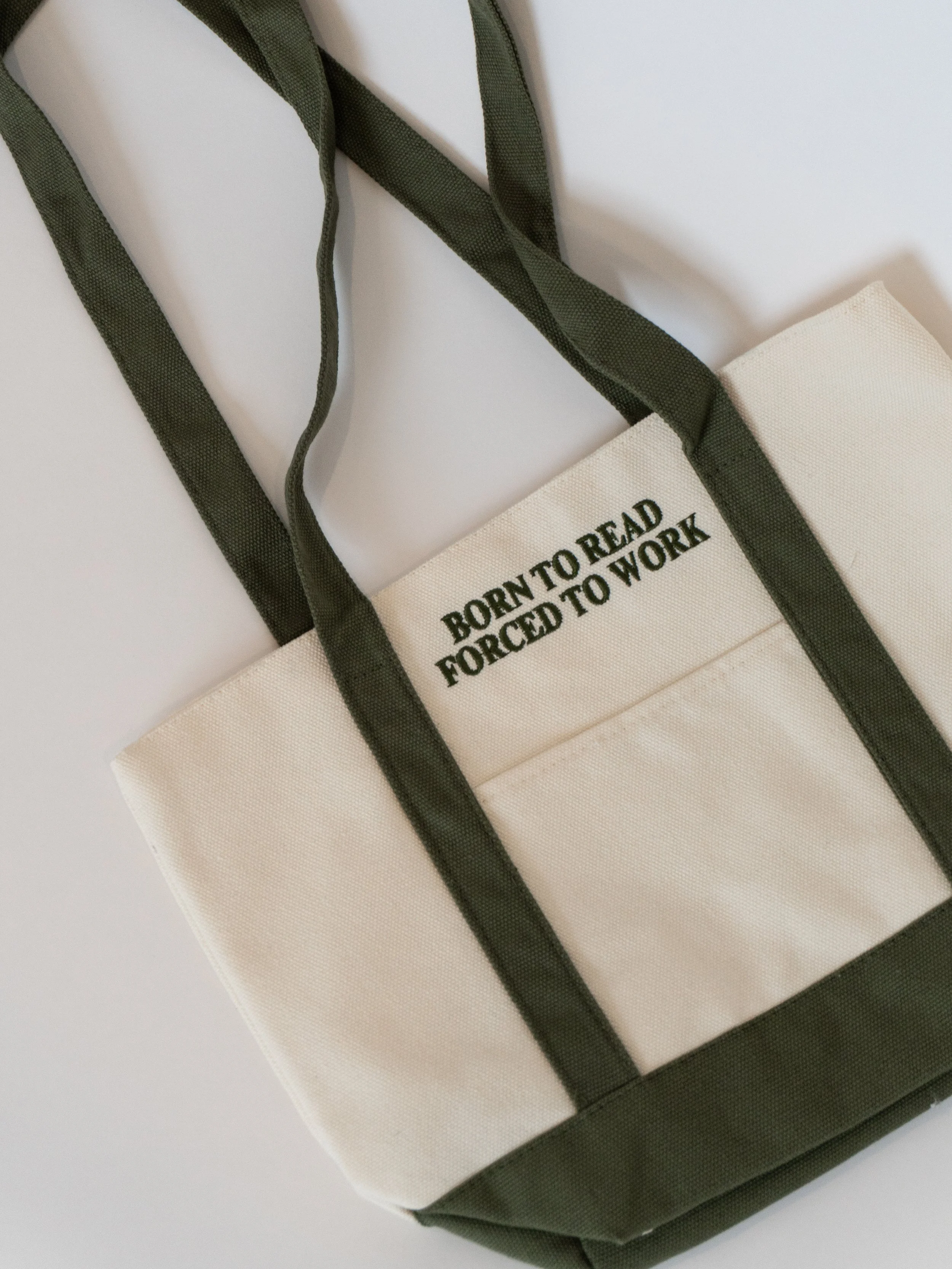 Born to Read Forced to Work embroidered canvas tote bag with green straps, a bookish tote for readers, bookstore trips, library hauls, and gifts for book lovers.