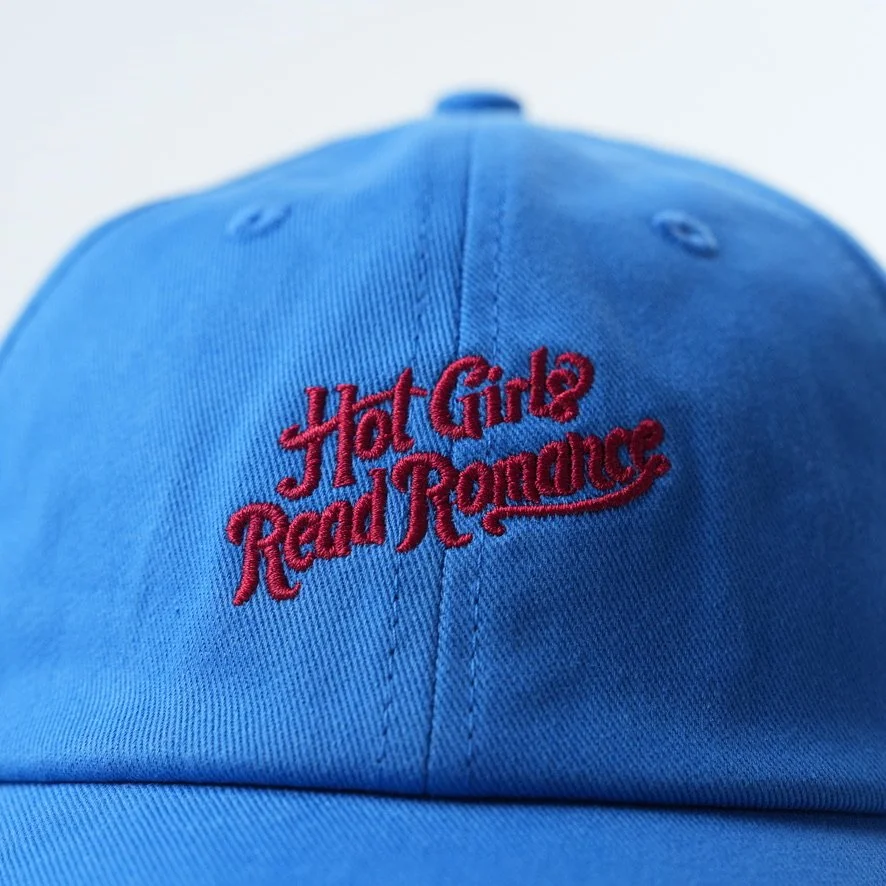 Light blue baseball cap embroidered with the phrase “Hot Girls Read Romance” in red script lettering.
