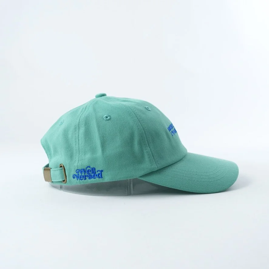 Mint green baseball cap embroidered with the phrase “SORRY I'M LATE I WAS READING” in bright blue lettering.