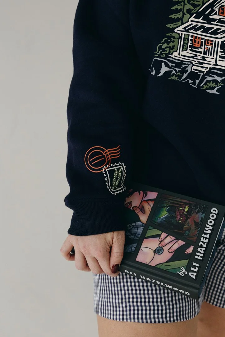 Navy mockneck sweatshirt featuring an illustration of Koen’s cabin inspired by Ali Hazelwood’s Mate, with a knot detail printed on the sleeve.