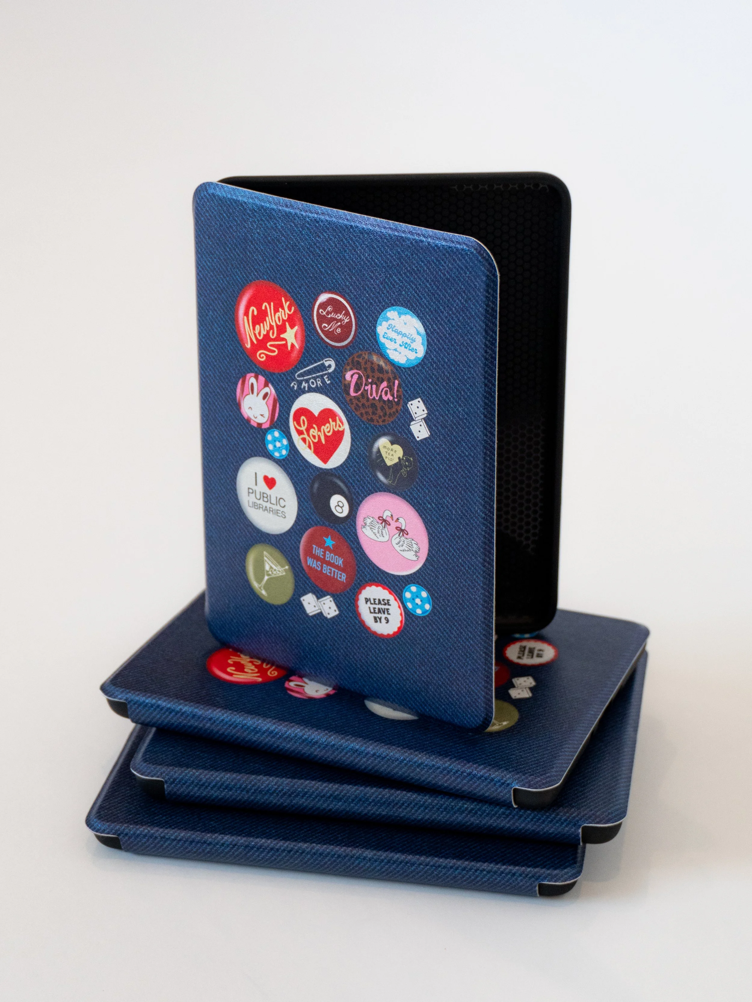 Stack of colorful Kindle cases featuring bookish designs and patterns, arranged together to showcase a variety of reader-inspired styles.