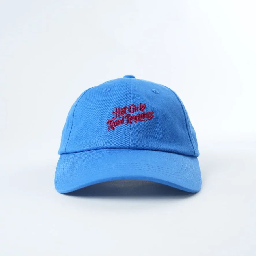 Light blue baseball cap embroidered with the phrase “Hot Girls Read Romance” in red script lettering.