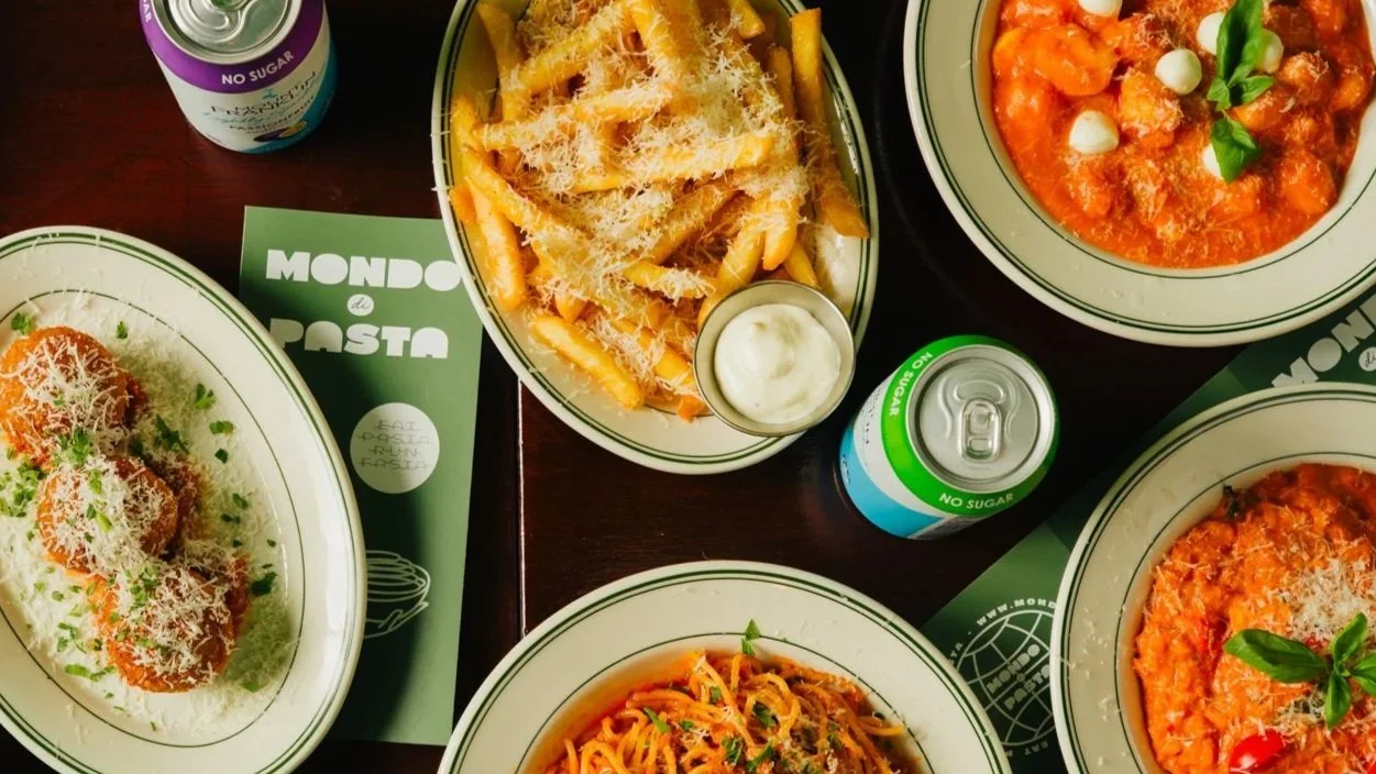 A table with several plates of Italian pasta dishes topped with grated cheese, a bowl of tomato sauce with basil and mozzarella, a plate of fried meatballs with grated cheese, and creamy pasta with vegetables at mondo di pasta in melbourne.