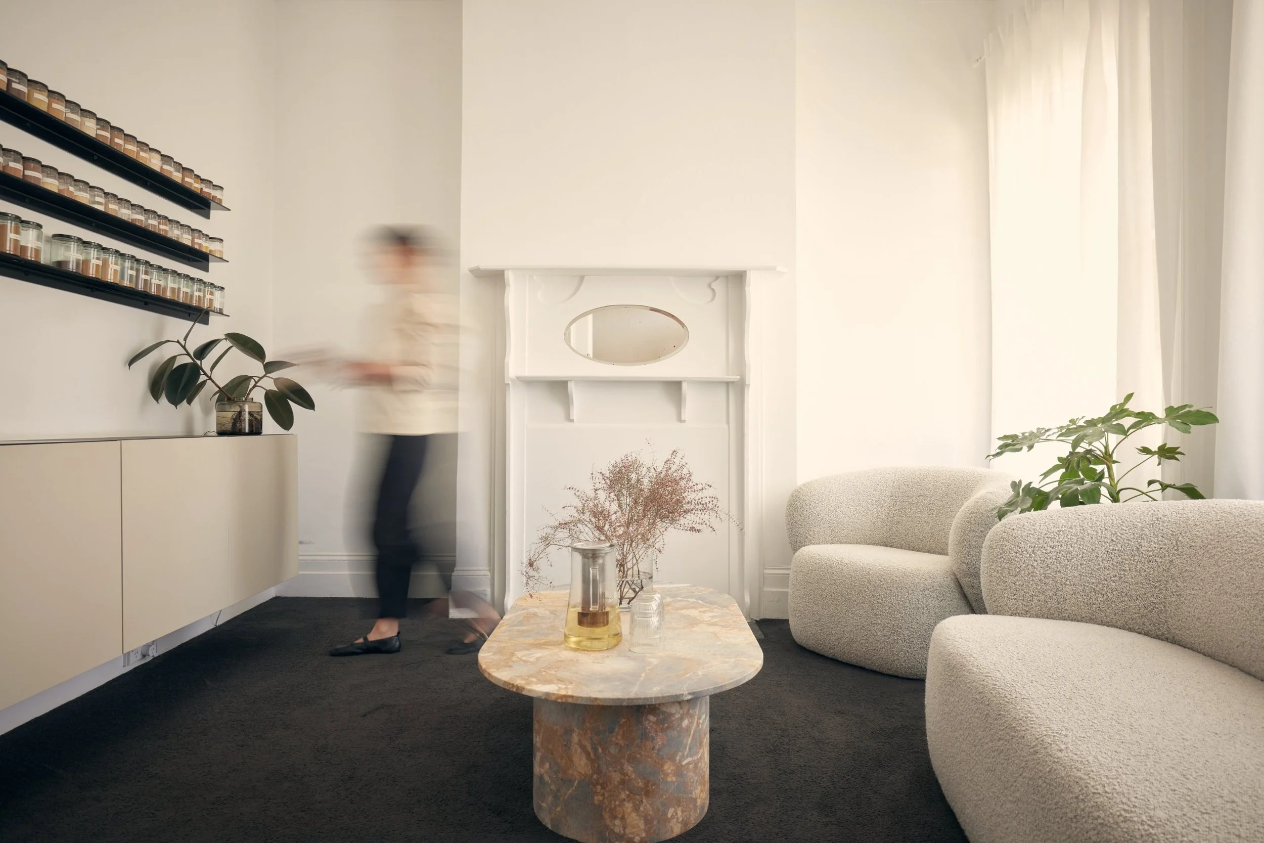 MRA reception with white sofa, marble coffee table, white walls, shelves with Chinese herbs, potted plants, and a fireplace