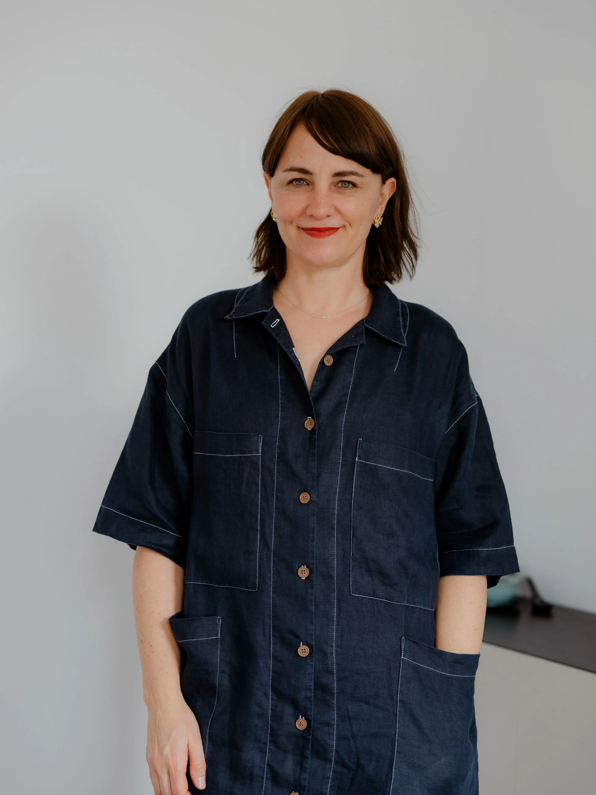 Practitioner, Kim, with short brown hair, wearing a dark denim button-up shirt, standing against a plain gray background, smiling at the camera.