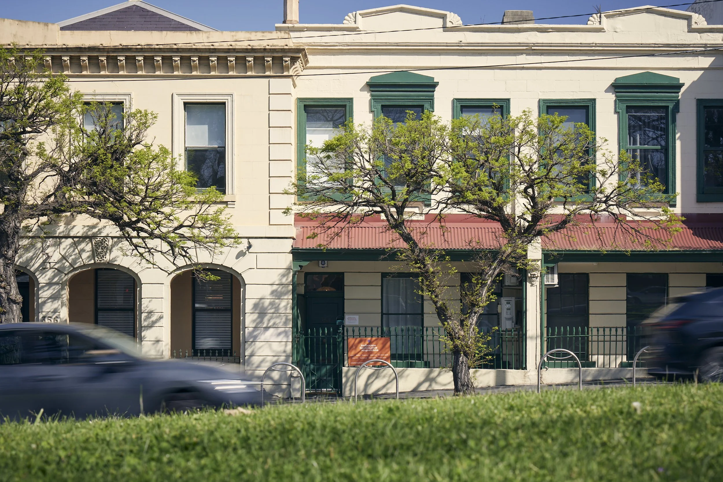 A row of buildings with trees in front, cars passing by in the street, and a clear blue sky.