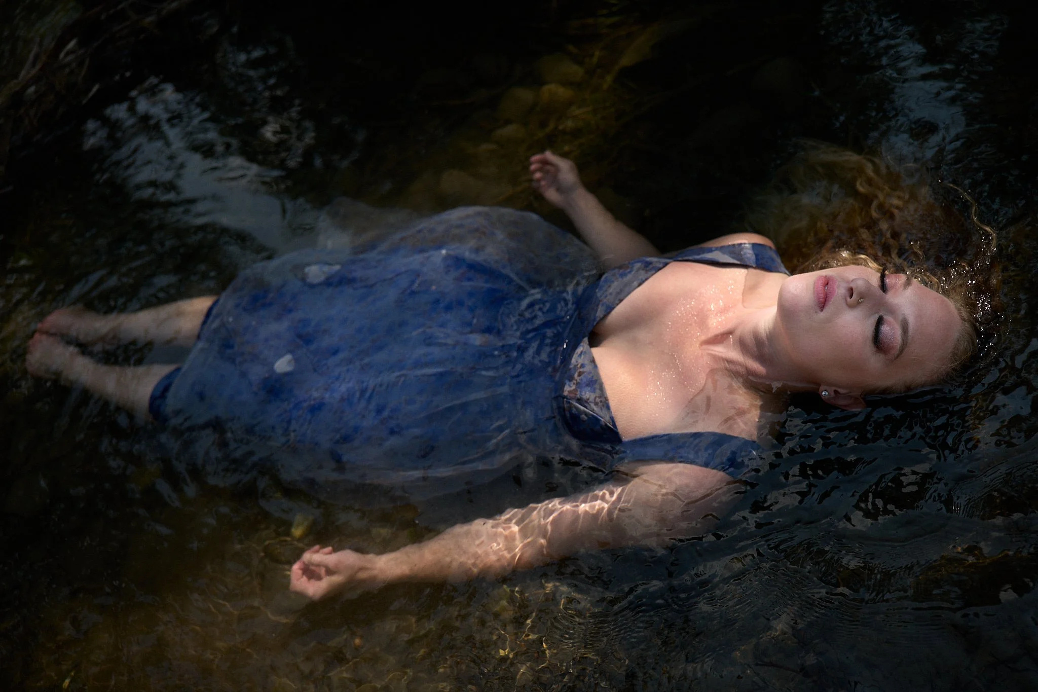 Woman in blue dress floating in water with eyes closed.
