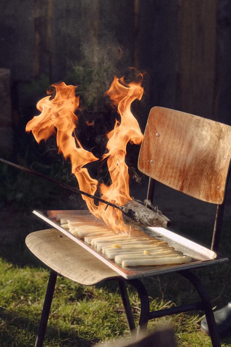 Een stoel met een bakplaat waarop asperges liggen en een vuur dat omhoog slaat.