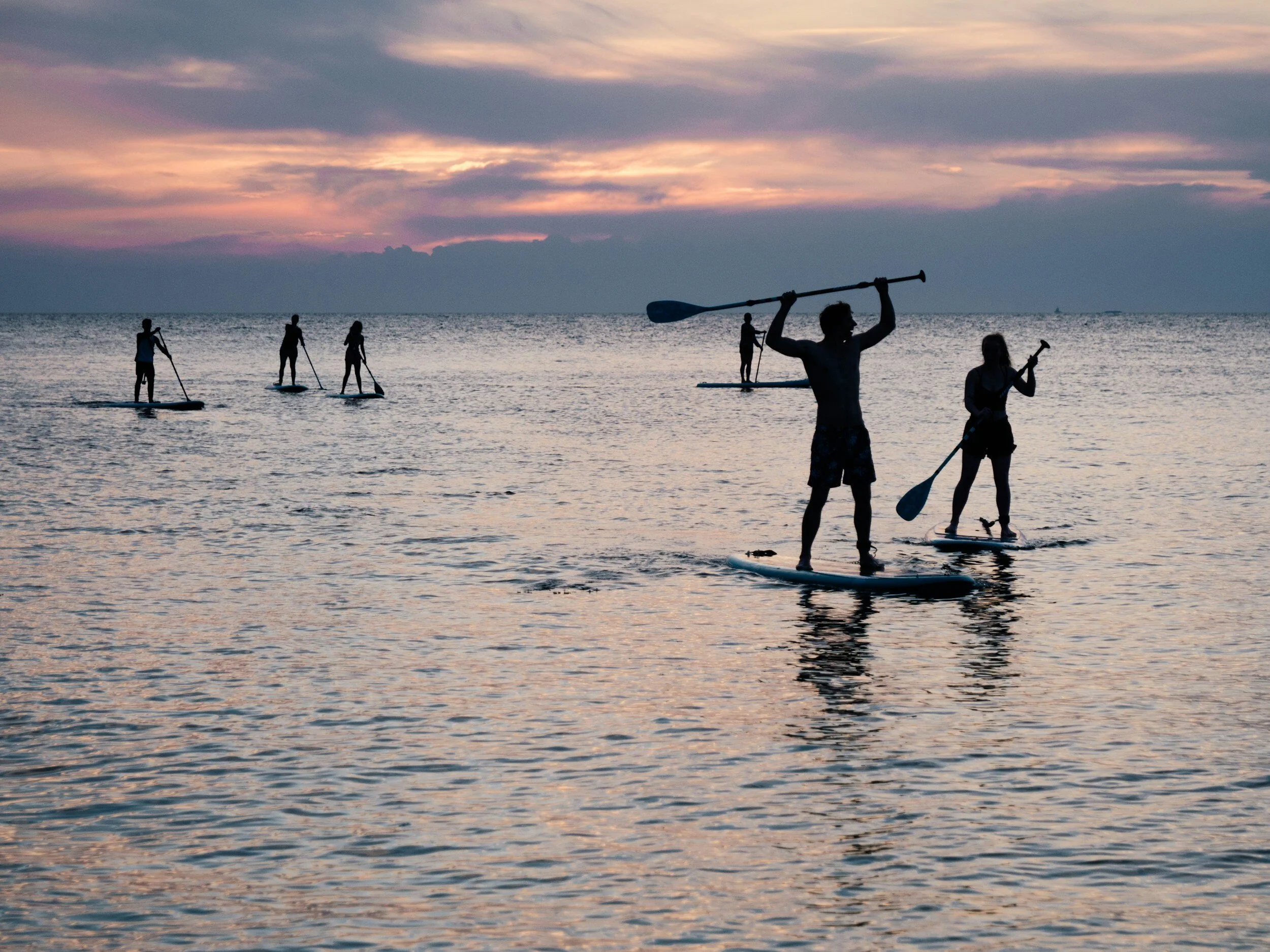 Personnes faisant du paddle sur un lac au coucher du soleil.