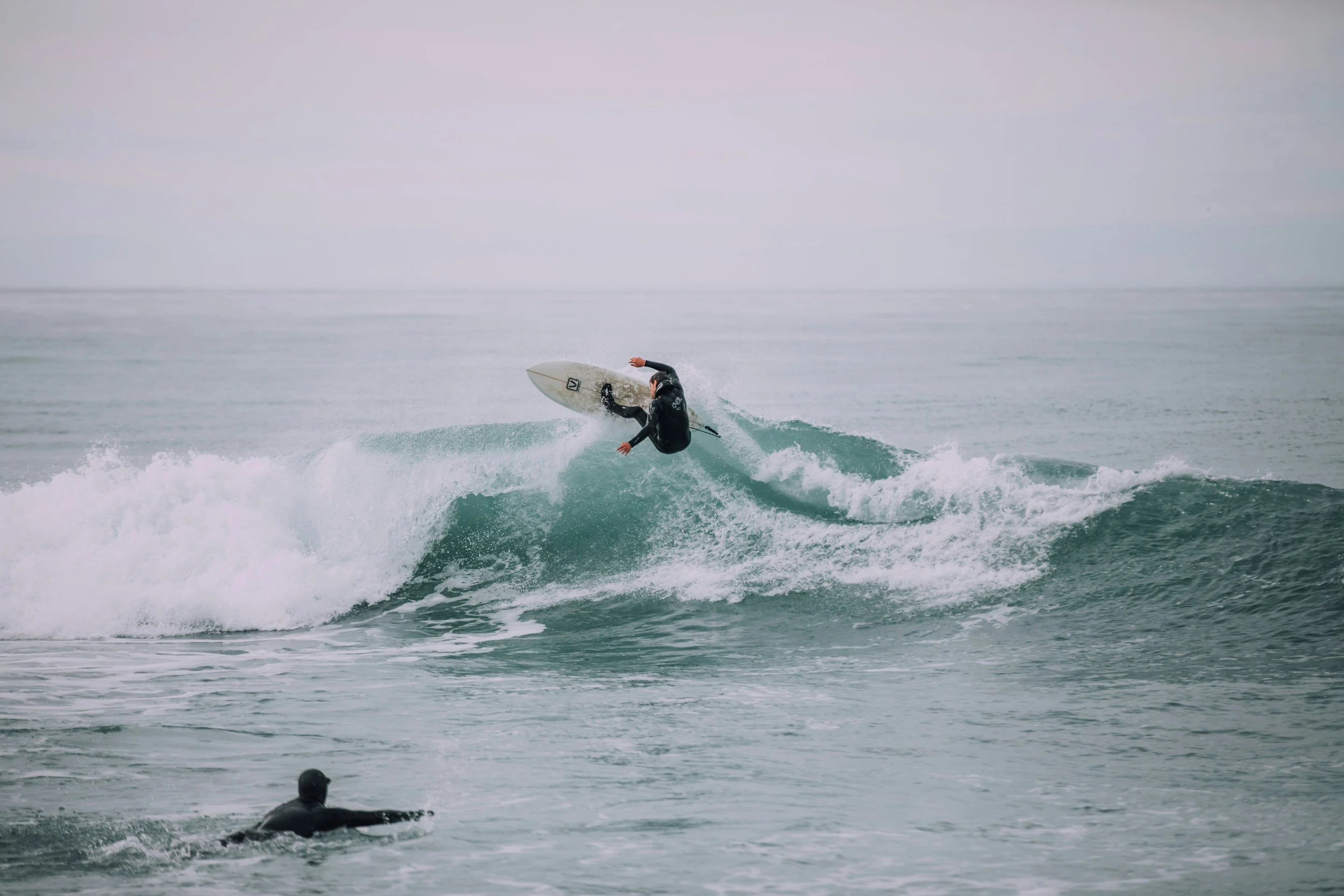 Deux surfeurs dans l'océan, l'un surfant sur une vague, l'autre flottant dans l'eau.