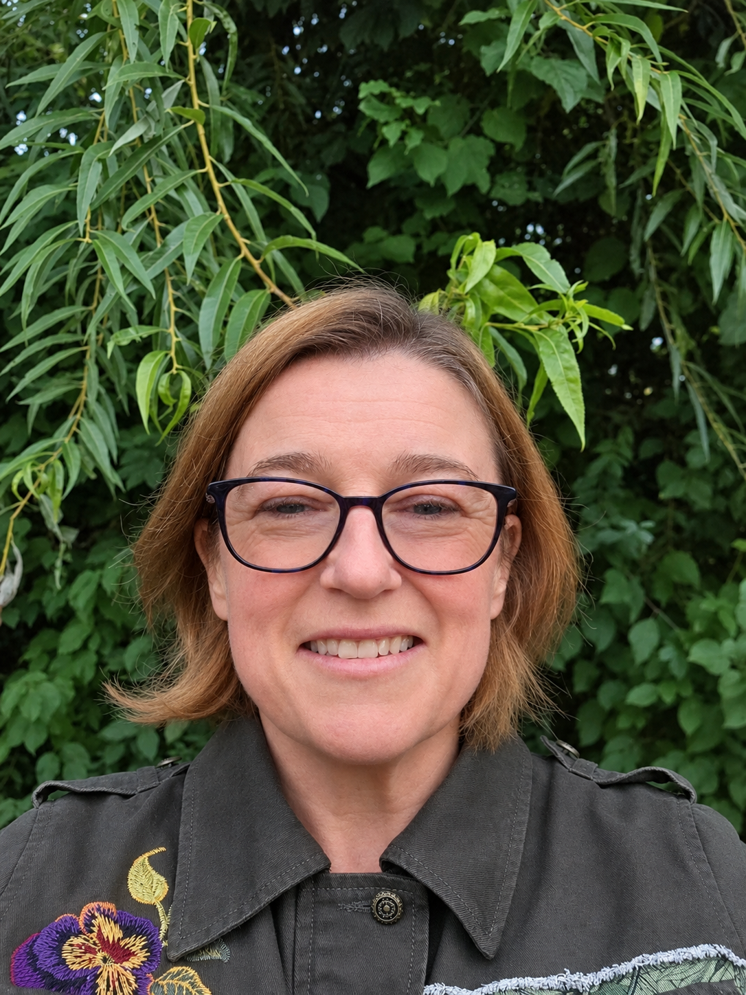 Profile photo of me smiling in front of some nice green shrubbery