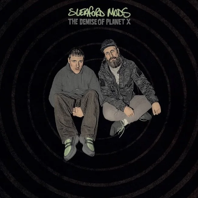 The cover of Sleaford Mods’ album The Demise of Planet X. this shows Jason Williamson and Andrew Fearn sitting down looking at the camera against a black background. The name of the band and the title of the album are written underneath them.