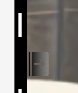 A gray rectangular sign with an arrow pointing to the right, mounted on a wall near a door, with a black vertical stripe on the left side.