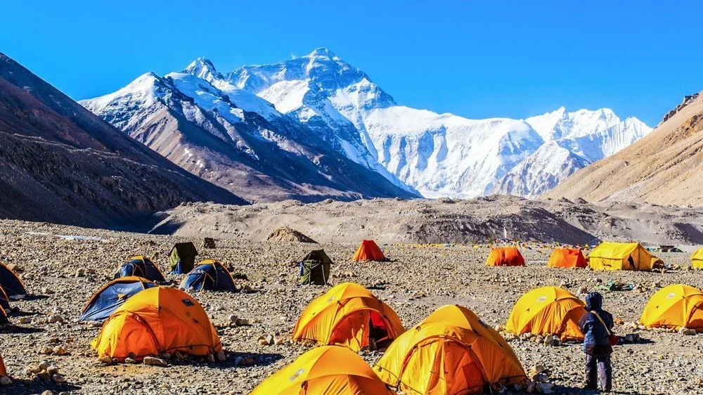Camping tents set beneath snowy mountains during an adventure trekking challenge