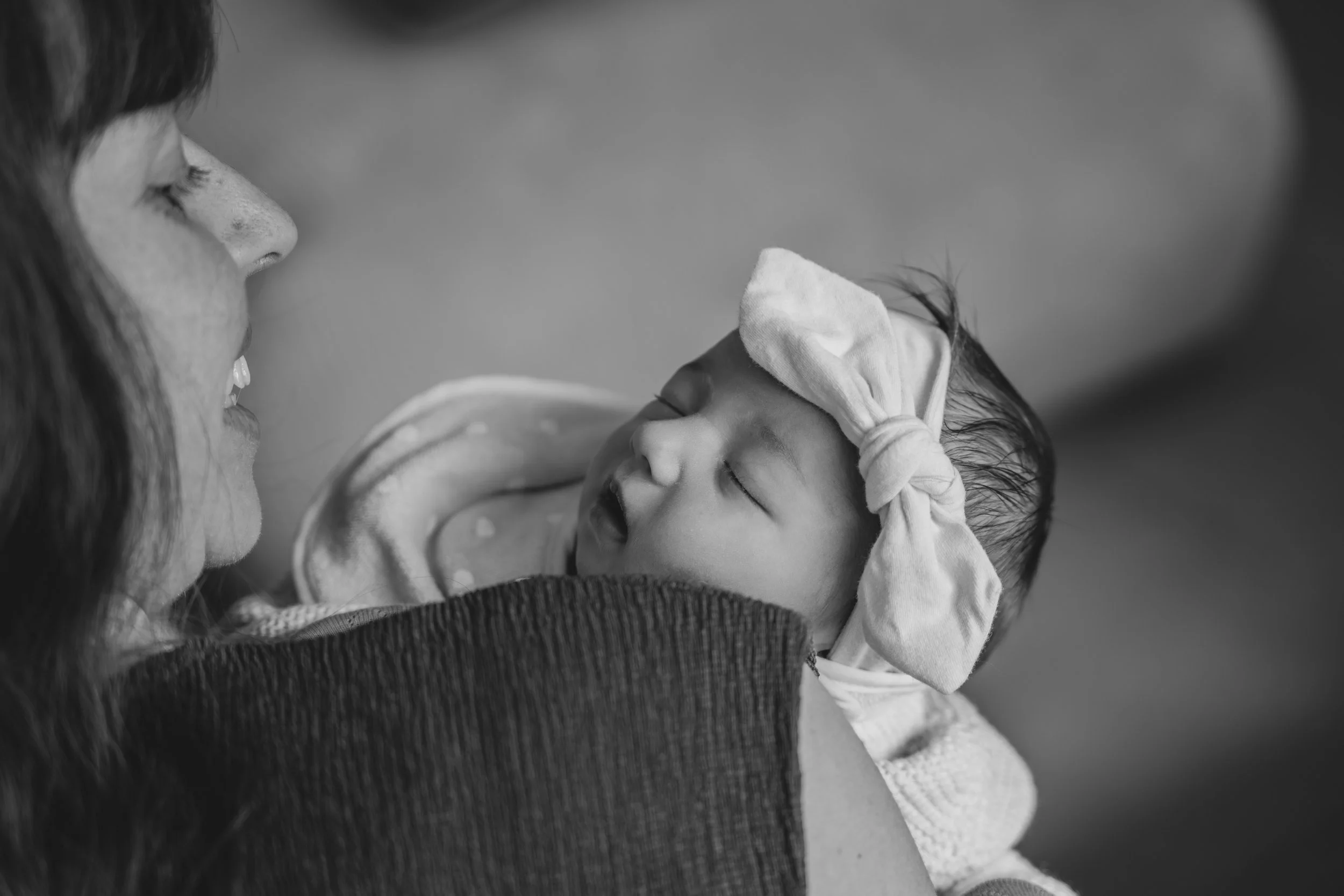 Une femme tient un bébé endormi contre elle, en noir et blanc.