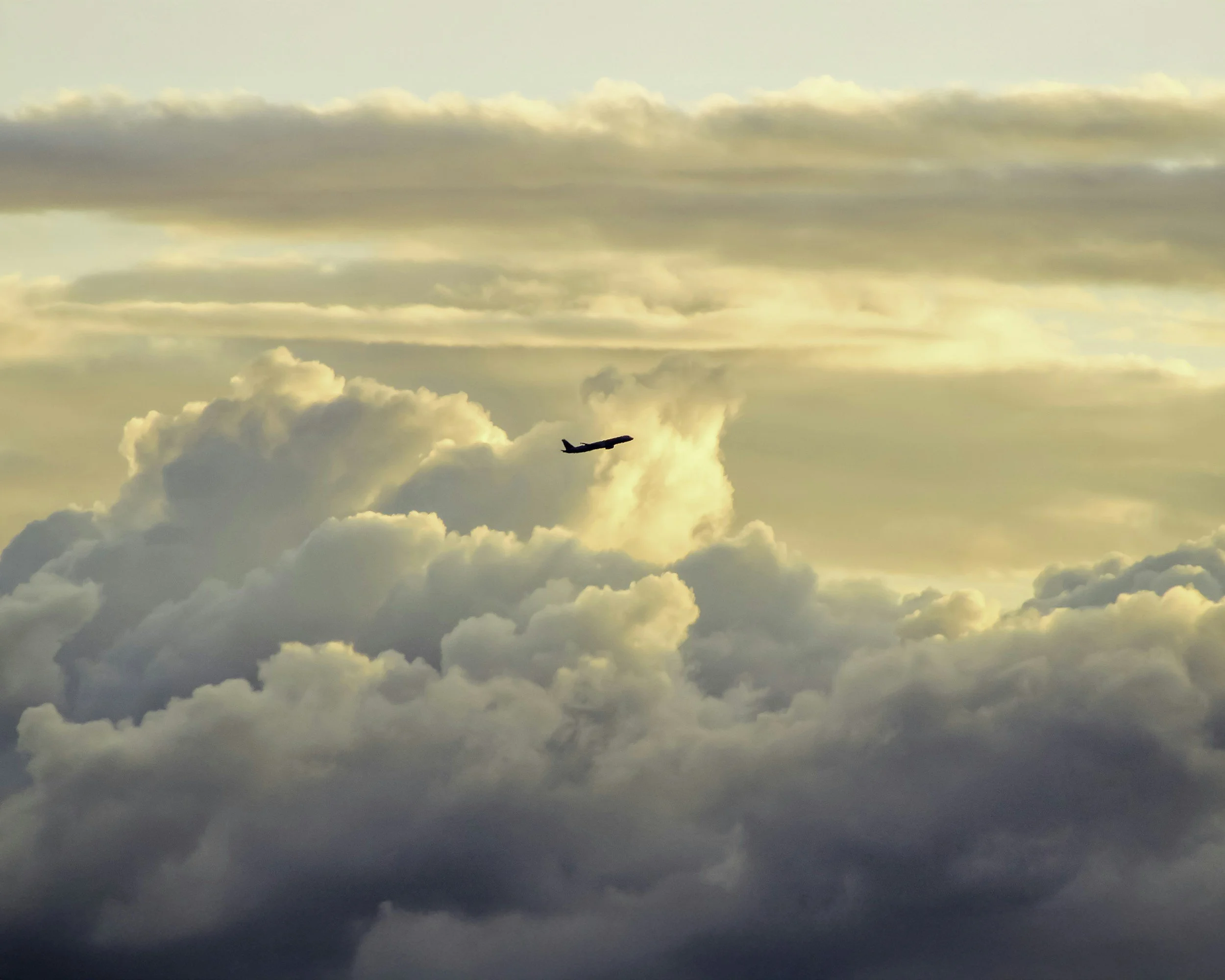Commercial passenger jet increasing altitude while surrounded by cumulus clouds.