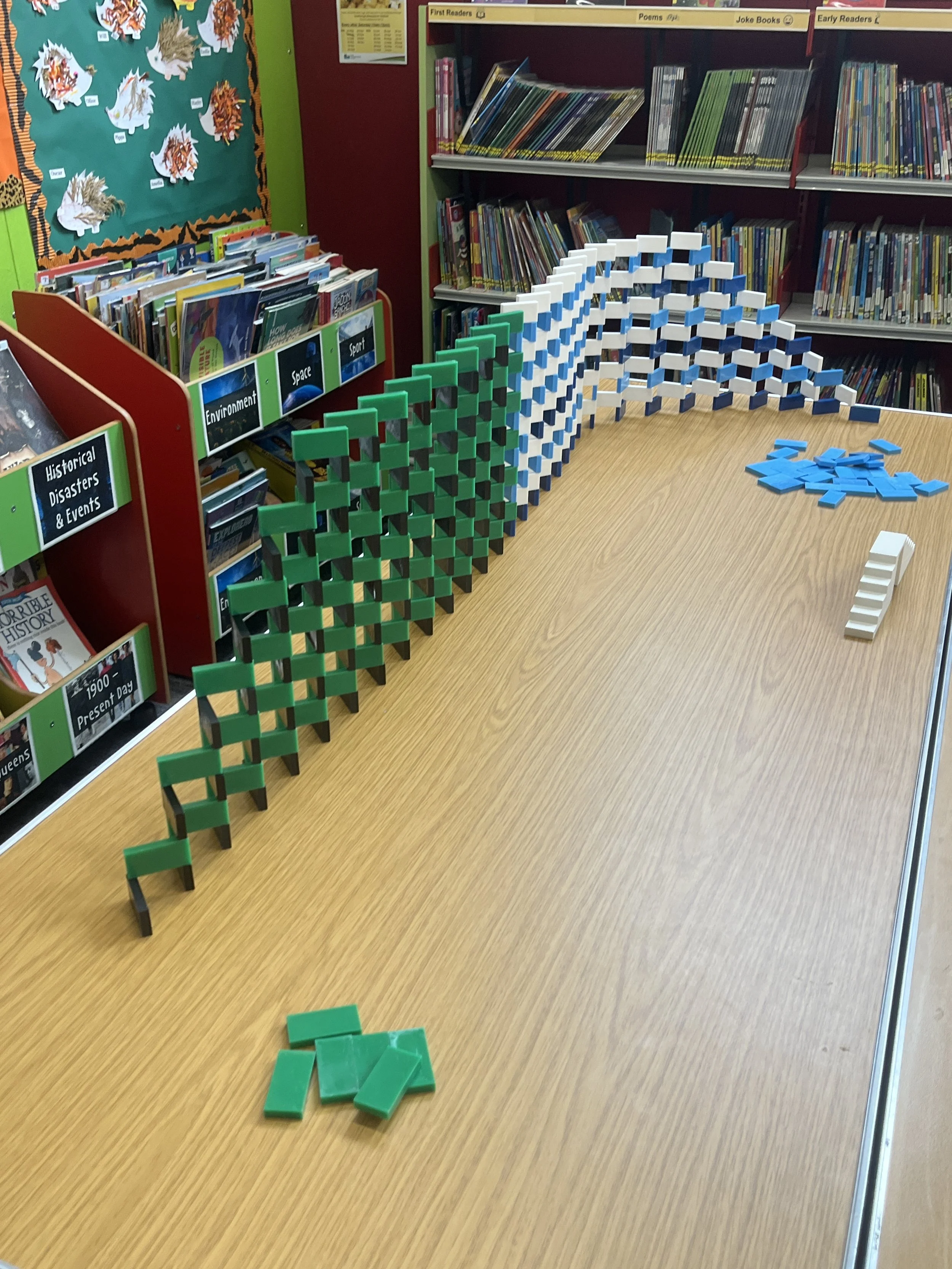 Library with a wooden table and colourful dominoes arranged in ascending order from green to white with blue in the middle, with some dominoes scattered on the table.