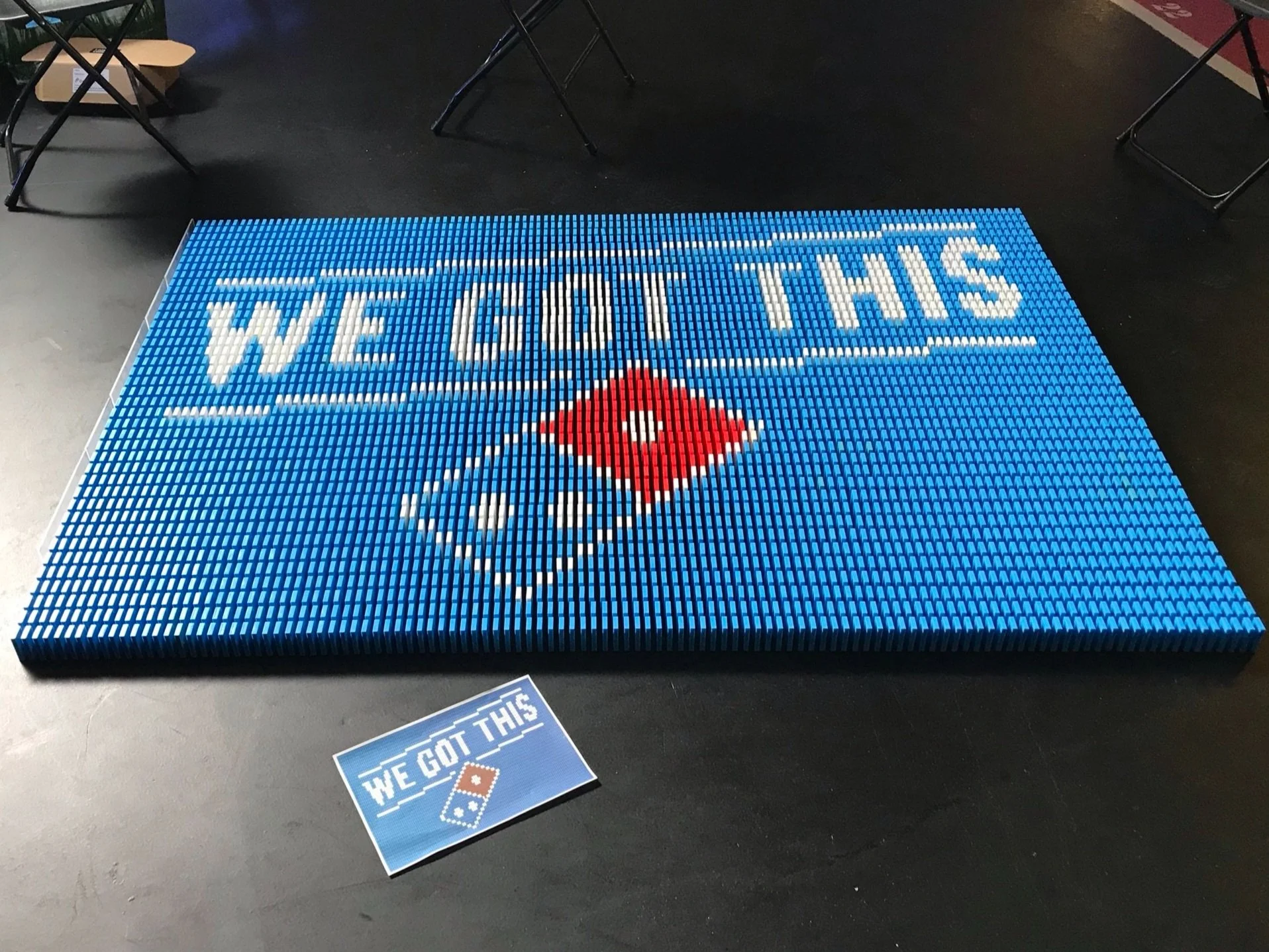 A large mosaic made of dominoes spelling out 'WE GOT THIS' with a red and blue domino tile representing the Domino's Pizza brand. A sign below repeats 'WE GOT THIS' with a domino graphic.