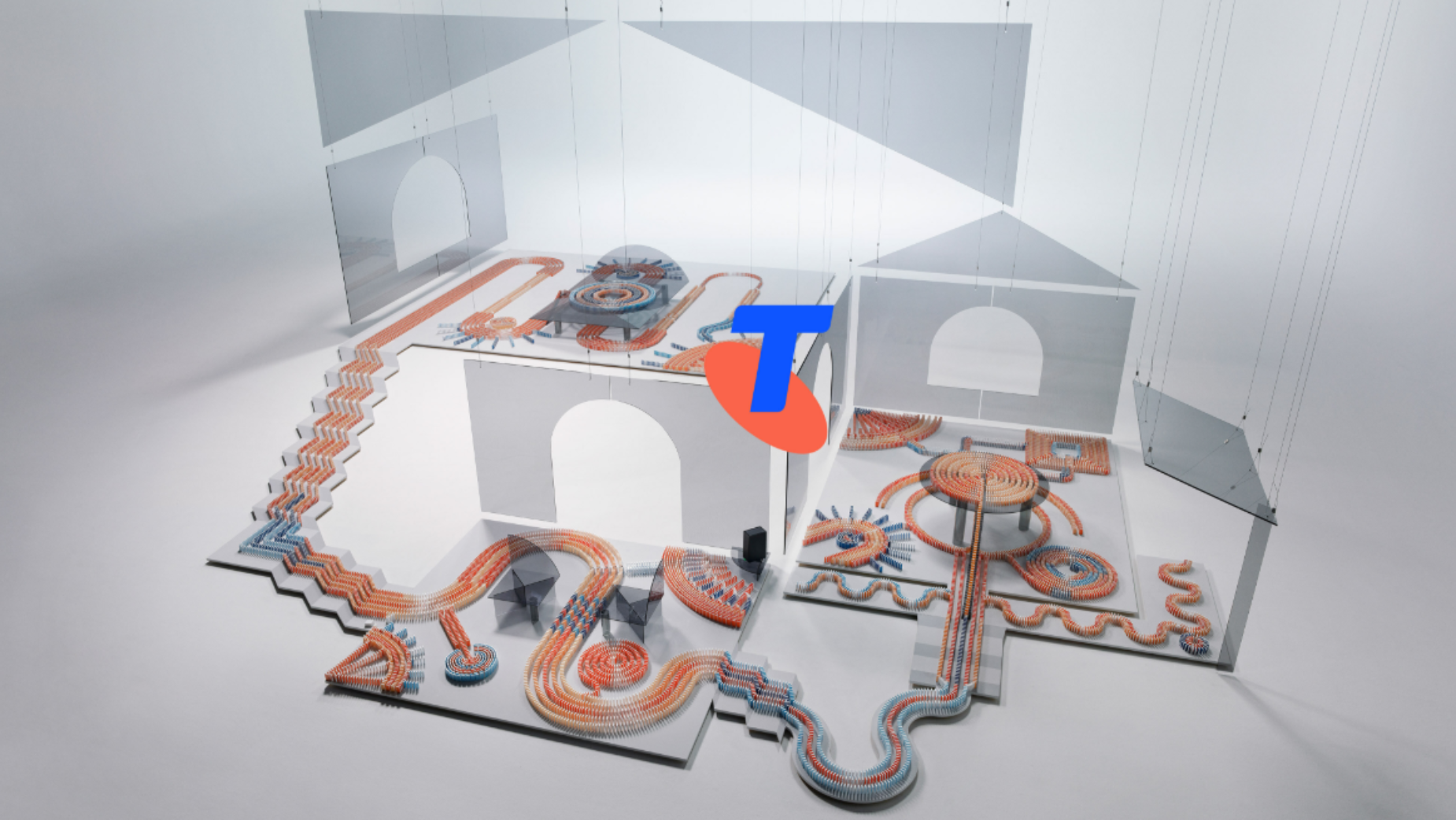 A detailed model of a two-story house with domino pathways, stairs, and abstract decorations. The house has open walls and the domino paths are orange, blue, and white.