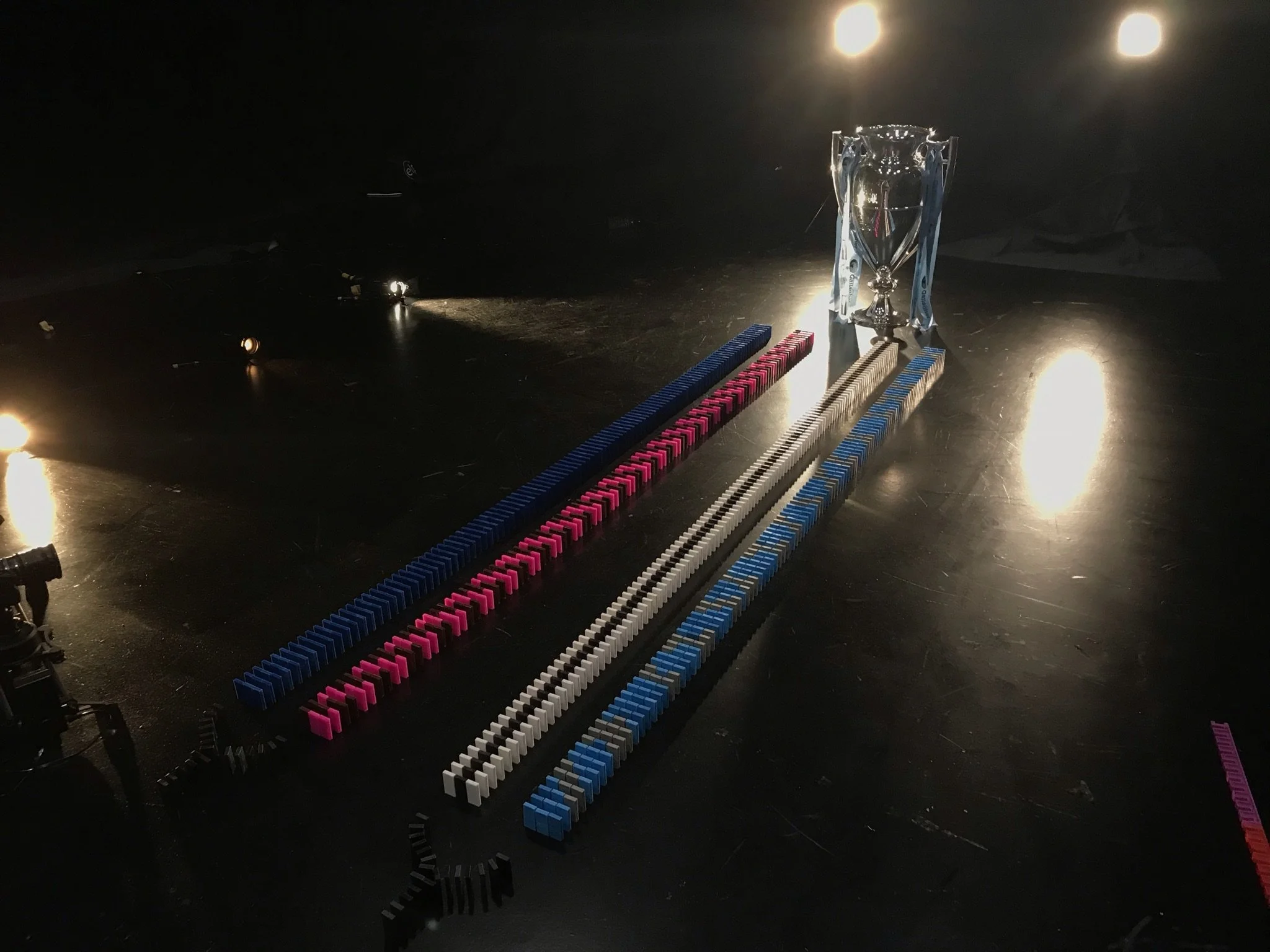 A small silver trophy is placed on a black surface among colourful dominoes arranged in patterns, with lights shining from above.