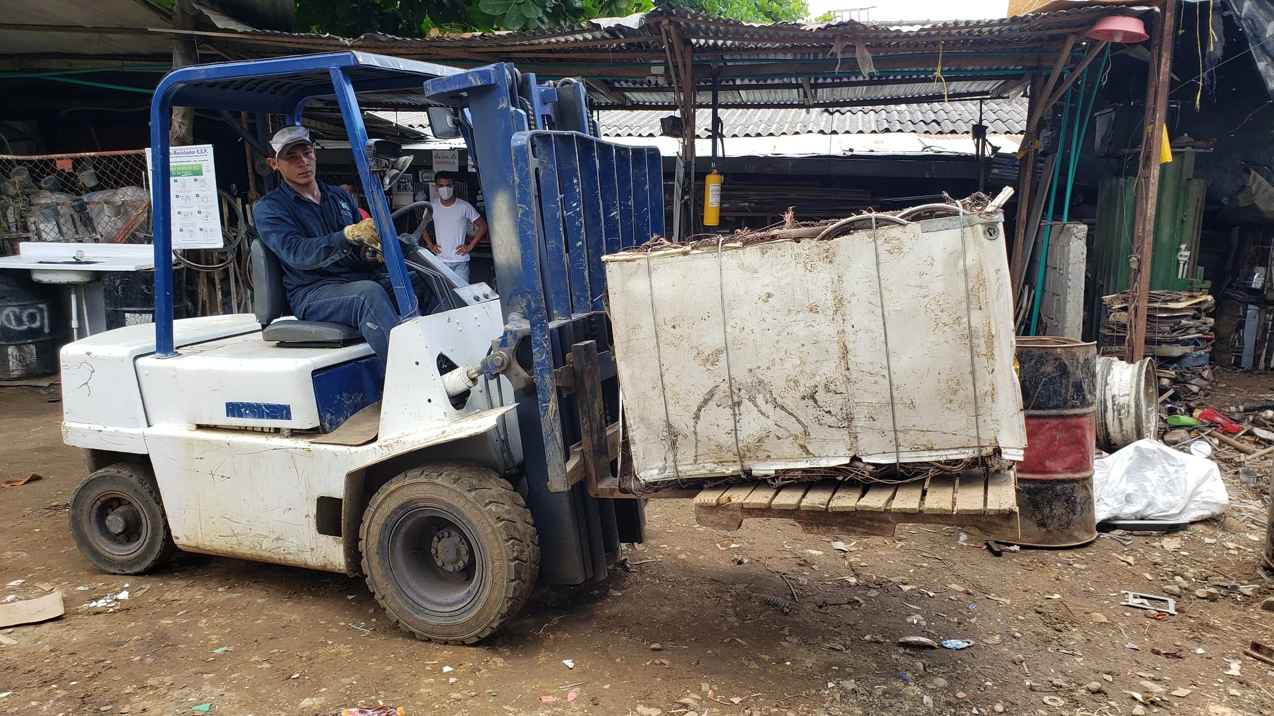 Persona operando un montacargas en un taller con herramientas y materiales de construcción en el fondo.