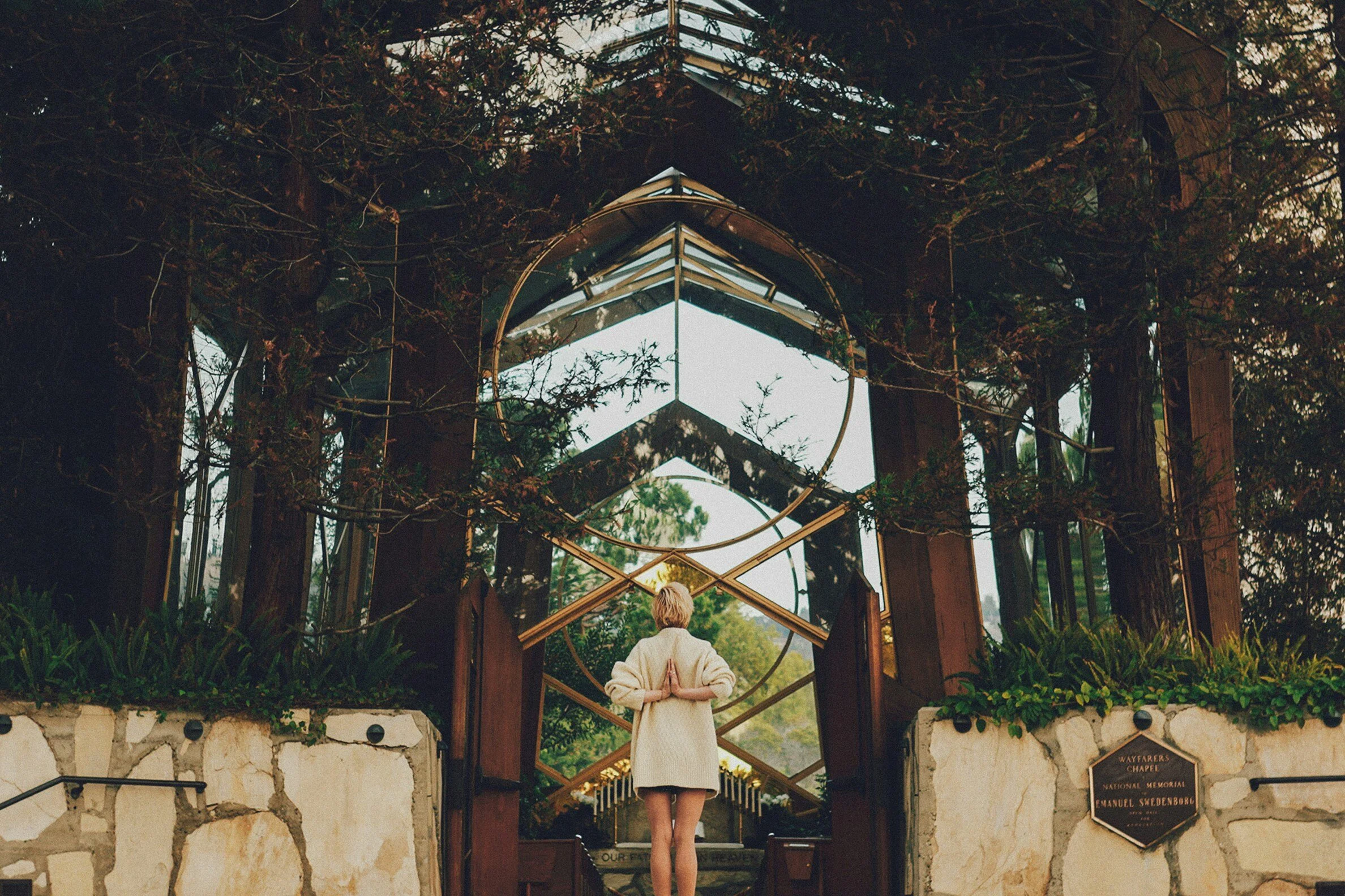 Person in front of modern glass chapel with trees and geometric design