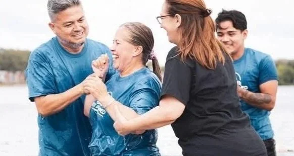 Group of people participating in a water-based activity outdoors, smiling and holding hands.