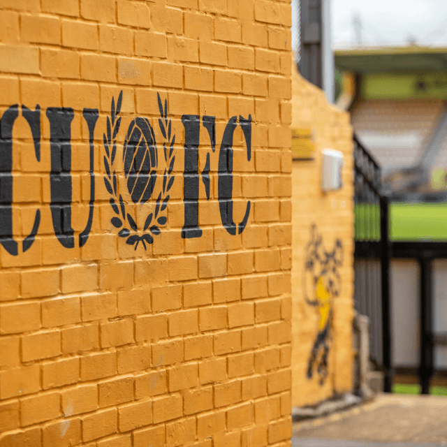 Close-up of a yellow brick wall with black stencil-style letters and a trophy laurel wreath design.
