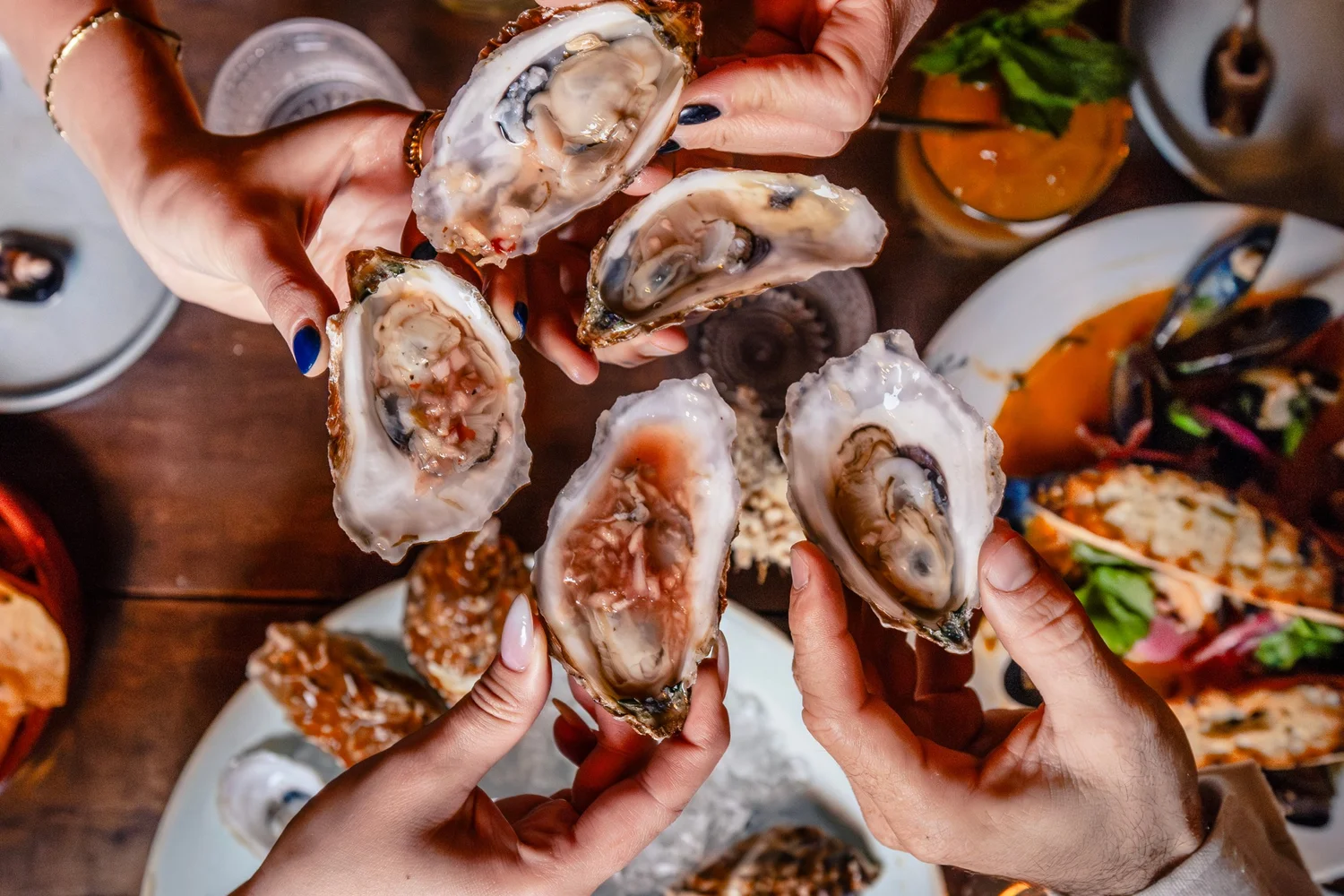 Oysters on the half shell, held up by four hands over the table